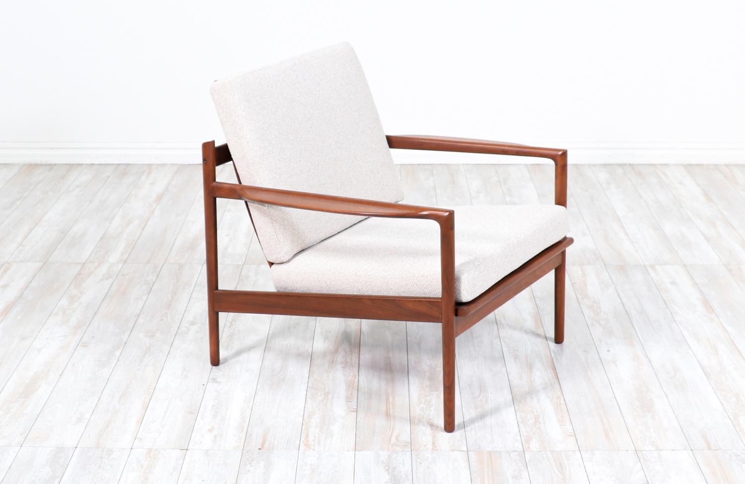 Stunning lounge chair designed by Ib Kofod-Larsen for Selig in Denmark circa 1960’s. This distinctive Danish modern design features a solid walnut wood frame with four large slats acting as the back rest plus comfortable, carved armrests. The