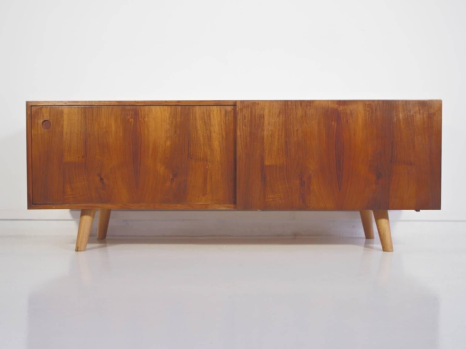 Ib Kofod-Larsen low sideboard made of hardwood, produced by Faarup Møbelfabrik in Denmark. Front with two sliding doors enclosing shelves in oak, cable outlet at the rear edge. Later fitted with round angled tapered legs made of solid oak.