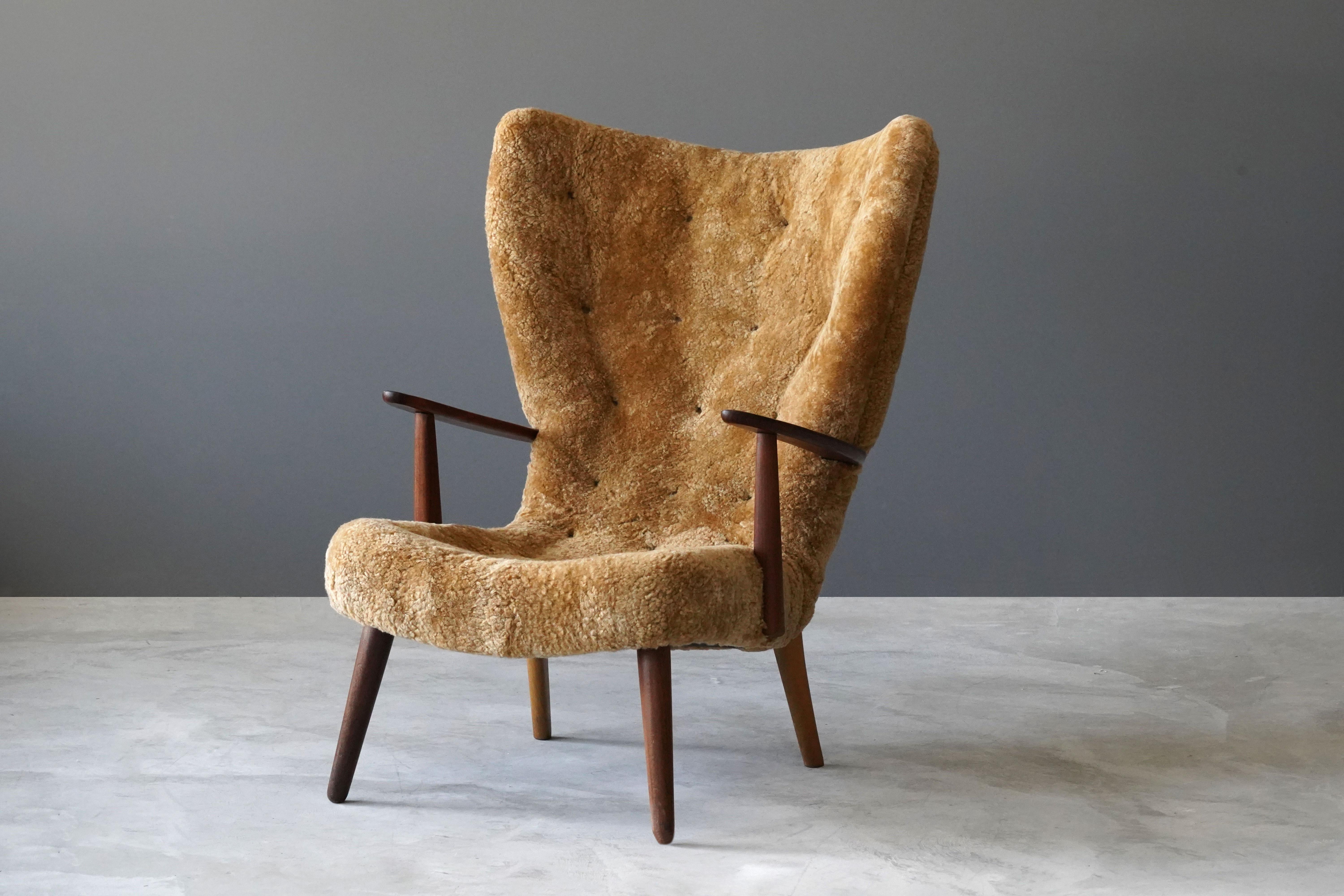 A high back lounge chair / armchair. Designed by Ib Madsen & Acton Schubell. Produced in Denmark, 1950s. The designers mixes typical mid-century aesthetics with organic form. 

Teak and beech frame, upholstered in brand new authentic lambskin /