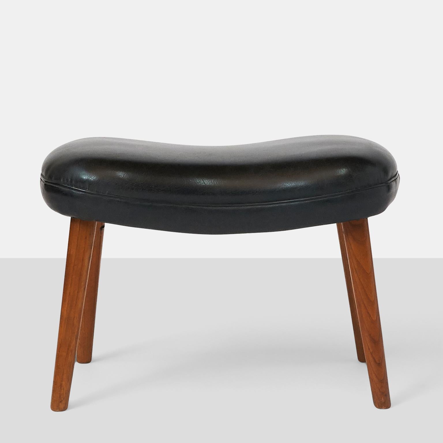 A rectangular shaped foot stool with black leather cushion seat and 4 tapered teak legs.