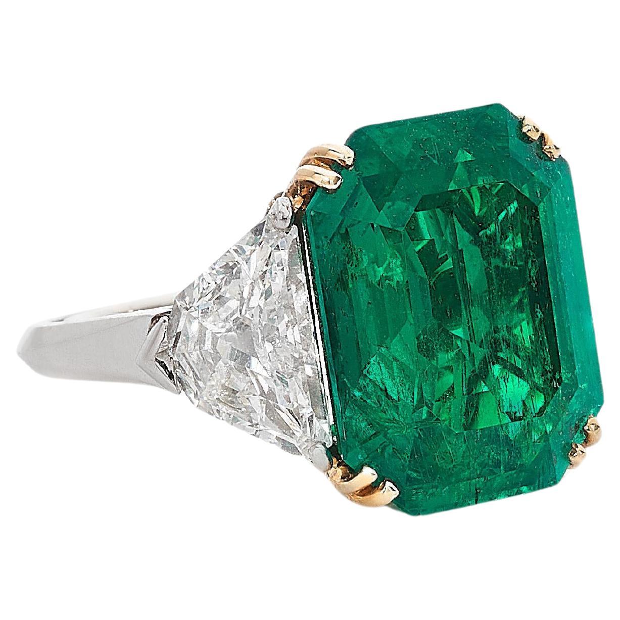 This exquisite ring features a ICA Certified 7.37 carat vivid green emerald as its stunning centerpiece, radiating a rich and captivating hue. Flanking the emerald are two shield-cut diamonds, adding a touch of brilliance and enhancing the ring's