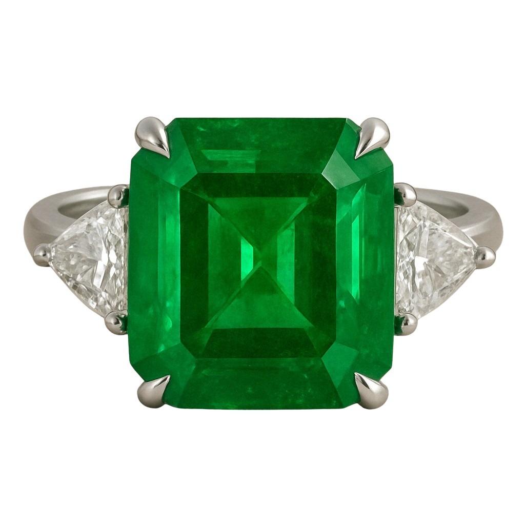 This exceptional three-stone ring features a mesmerizing 5.49 carat natural emerald of nearly square proportions, certified by ICA GemLab as originating from Zambia. Exhibiting an intense vivid green hue, the emerald is masterfully cut in a step-cut