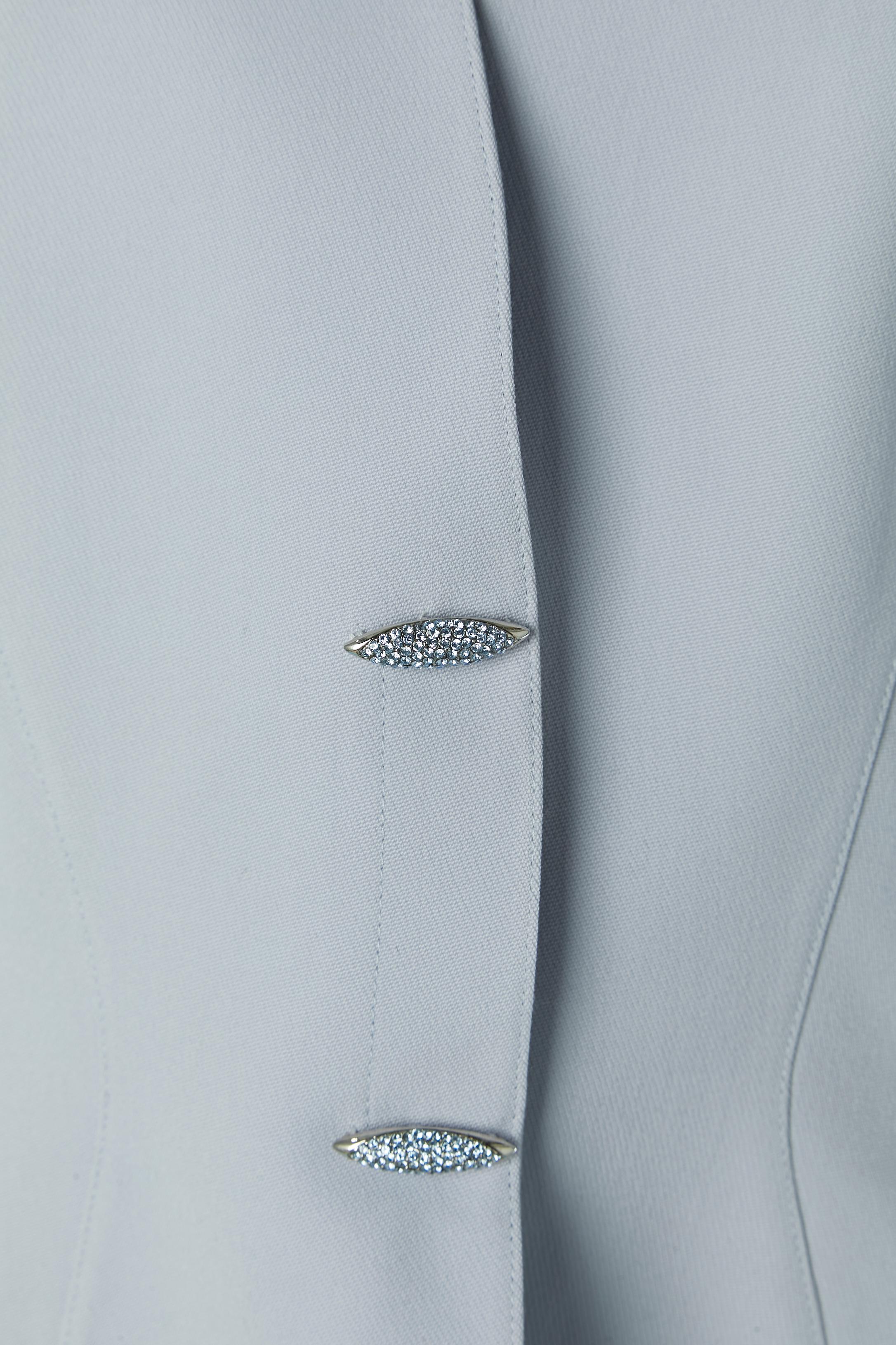 Veste bleu glacier à simple boutonnage, ornée de strass. Composition du tissu principal : laine . Doublure probablement en acétate ou en rayonne. Fermeture à bouton-pression sur le milieu du devant. Fendu sur le devant côté bas + sur l'encolure.
