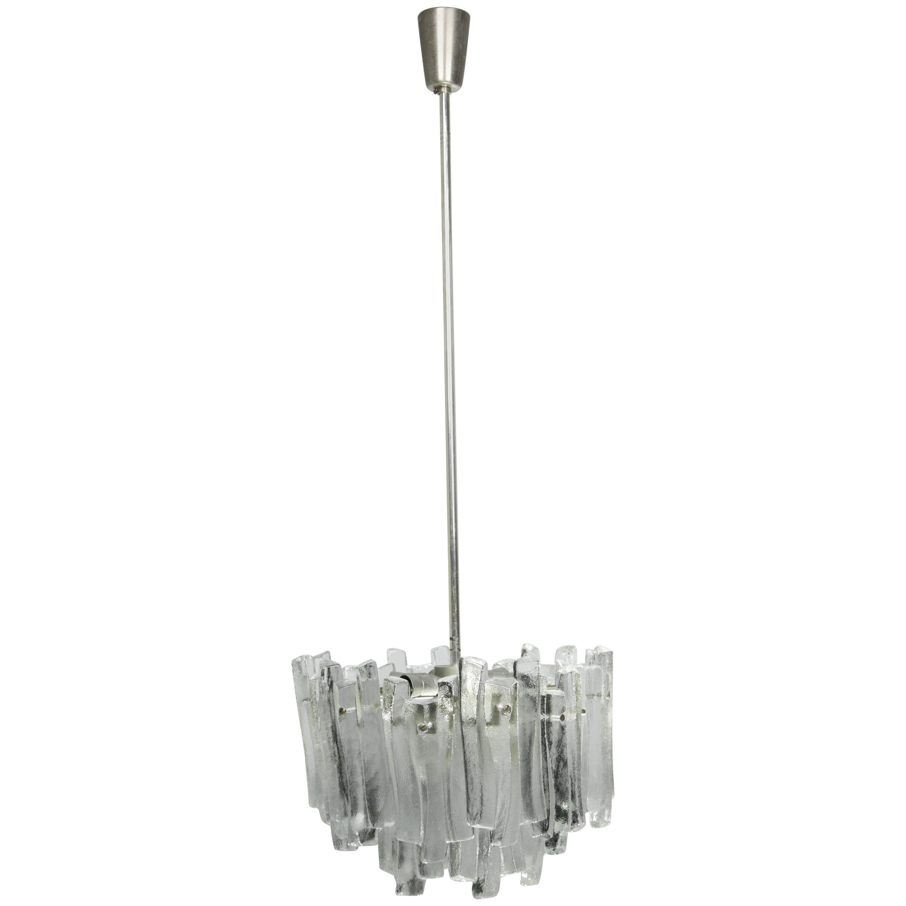 Ice glass chandelier, 1960, Kalmar, Austria
Metal frame holding 18 pieces of thick ice looking glass with a matte organically shape spread out on two rows, the inside of the glass is clear and flat, there is seven original European light sources