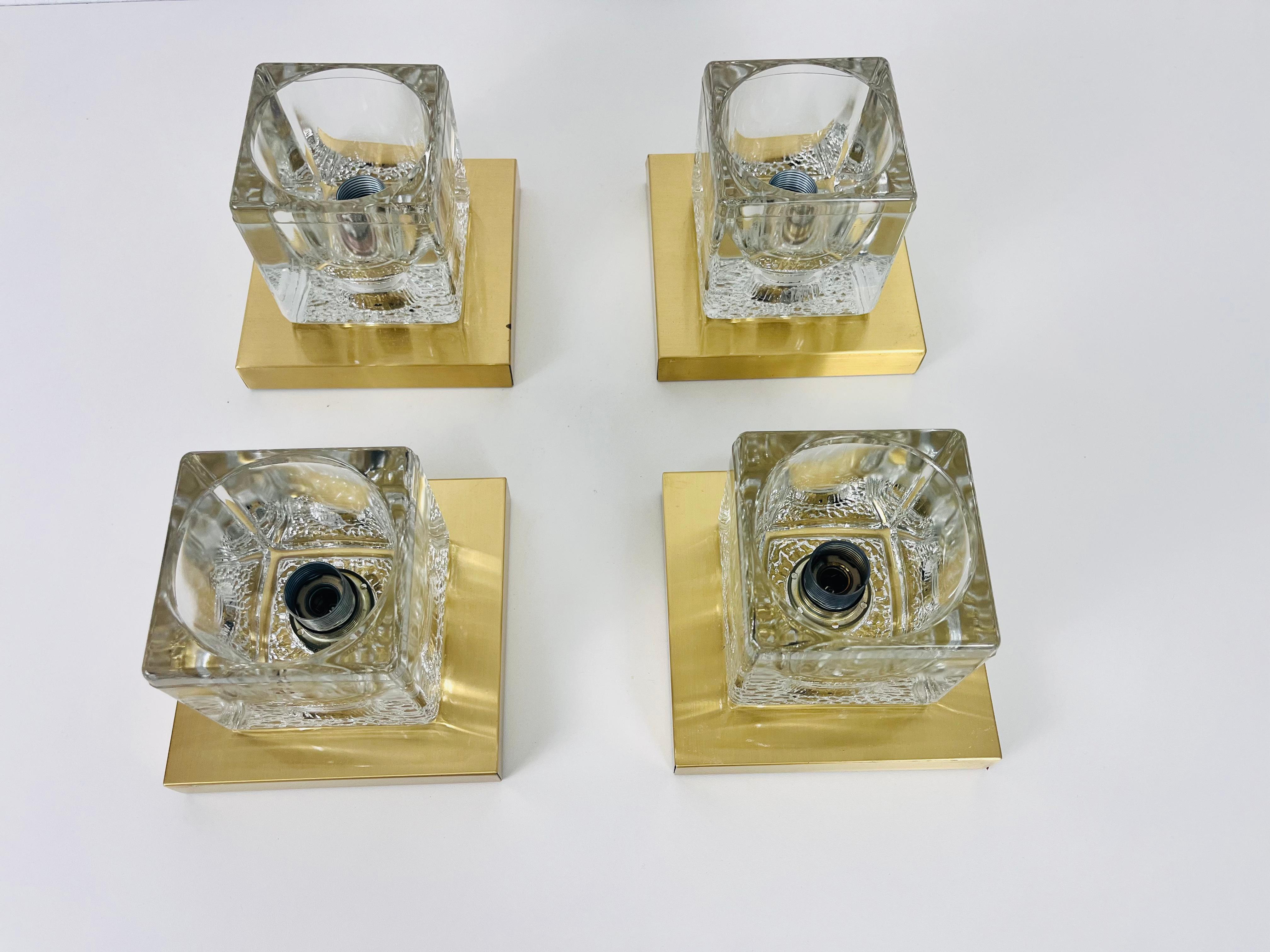 A beautiful set of wall lamps by Peill & Putzler made in Germany in the 1970s. They have a cube shape and are made of transparent ice glass with a brass base. The lightings can also used as flushmounts or table lamps. They are in very good vintage