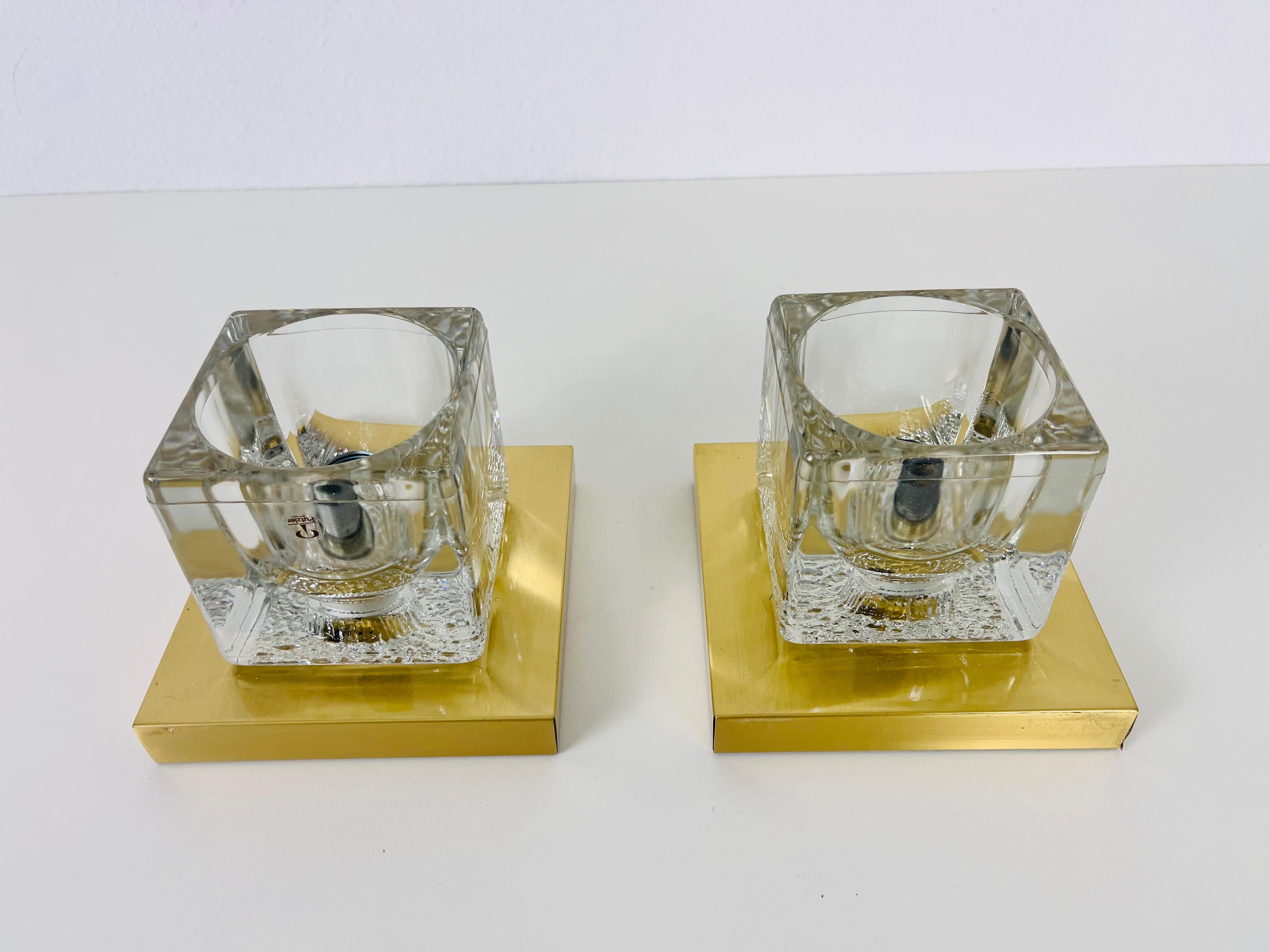 A beautiful set of wall lamps by Peill & Putzler made in Germany in the 1970s. They have a cube shape and are made of transparent ice glass with a brass base. The lightings can also used as flushmounts or table lamps. They are in very good vintage