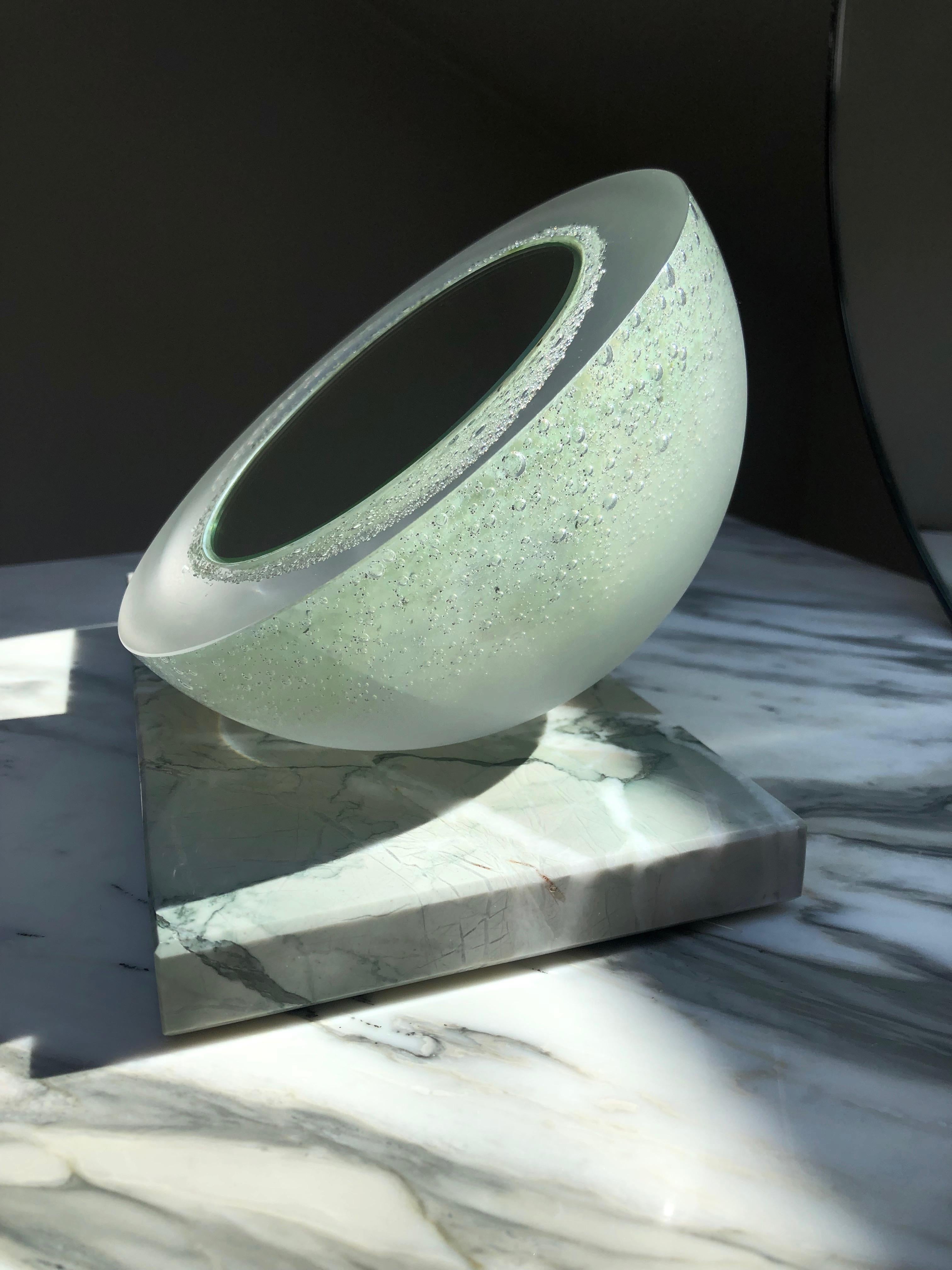 'Ice Queen' vanity / make-up mirror in mint green mouth-blown glass setting on a polished Verde Antigua marble base on soft glides. Thick blown glass shell shows variations from lusterous polished to matt glass at the bottom part, so the mirror can