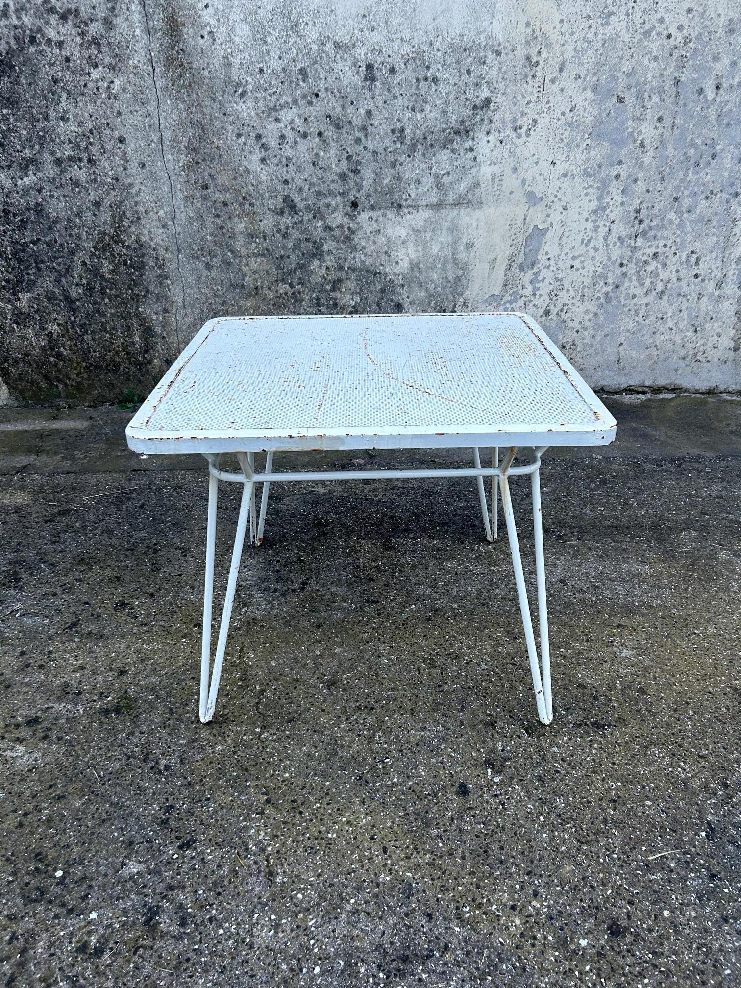 Vier V-förmige Beine, die aus einem einzigen Stück Eisenrohr geformt wurden, sind oben an die Hauptstruktur geschweißt, wo sie sich nach außen biegen, um die Tischplatte zu tragen. Es besteht aus einem quadratischen Lochblech mit abgerundeten Ecken,