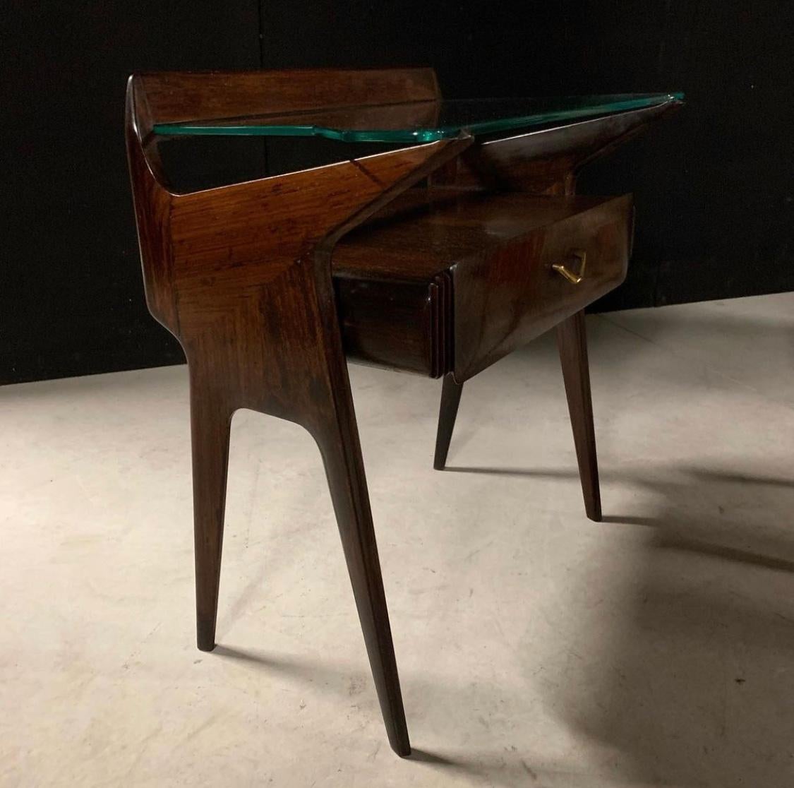 Pair of bedside tables in the manner of Ico Parisi and Vittorio Dassi.

Featuring split level glass and wood tabletops

Single drawer with etched ribbing at sides. V-shaped pull handle in brass. 

Glass shelf sits within channel at back