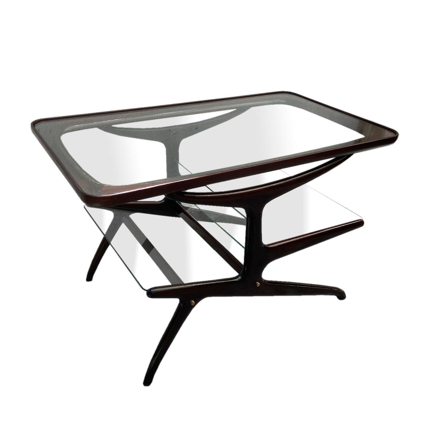 A complex tree structure with asymmetrical arms characterizes the table. The upper branches support the large rectangular glass top while the two underlying arms hold 2 glass shelves divided by a vertical rod and used as a magazine rack.