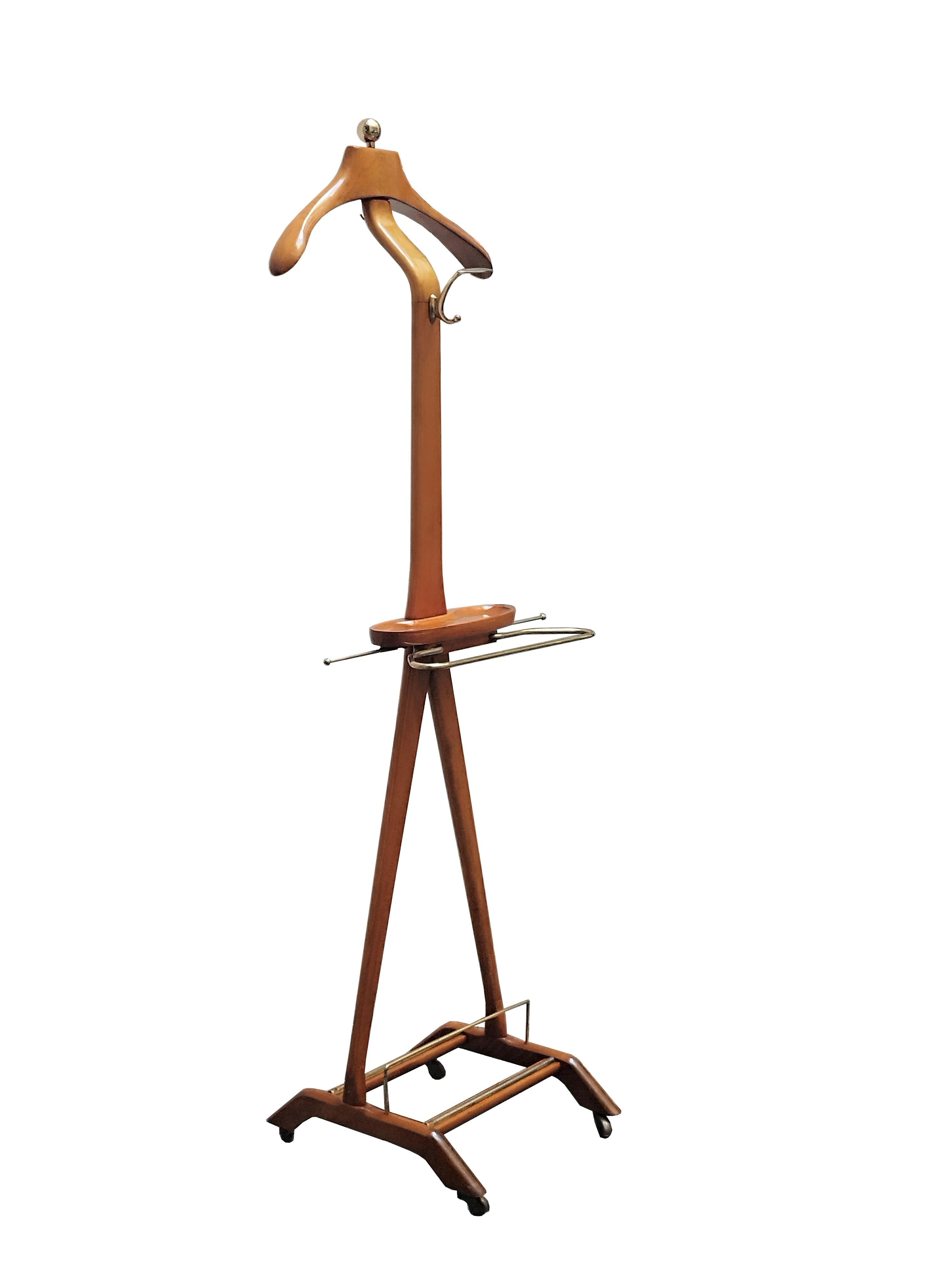 An elegant gentleman's servant made and designed in Italy around 1960 by Ico Parisi for Fratelli Reguitti, the wood and brass servant , stands on a sculptural X-shaped frame with lower casters; it features a coat hanger, tidy tray, trouser rod and
