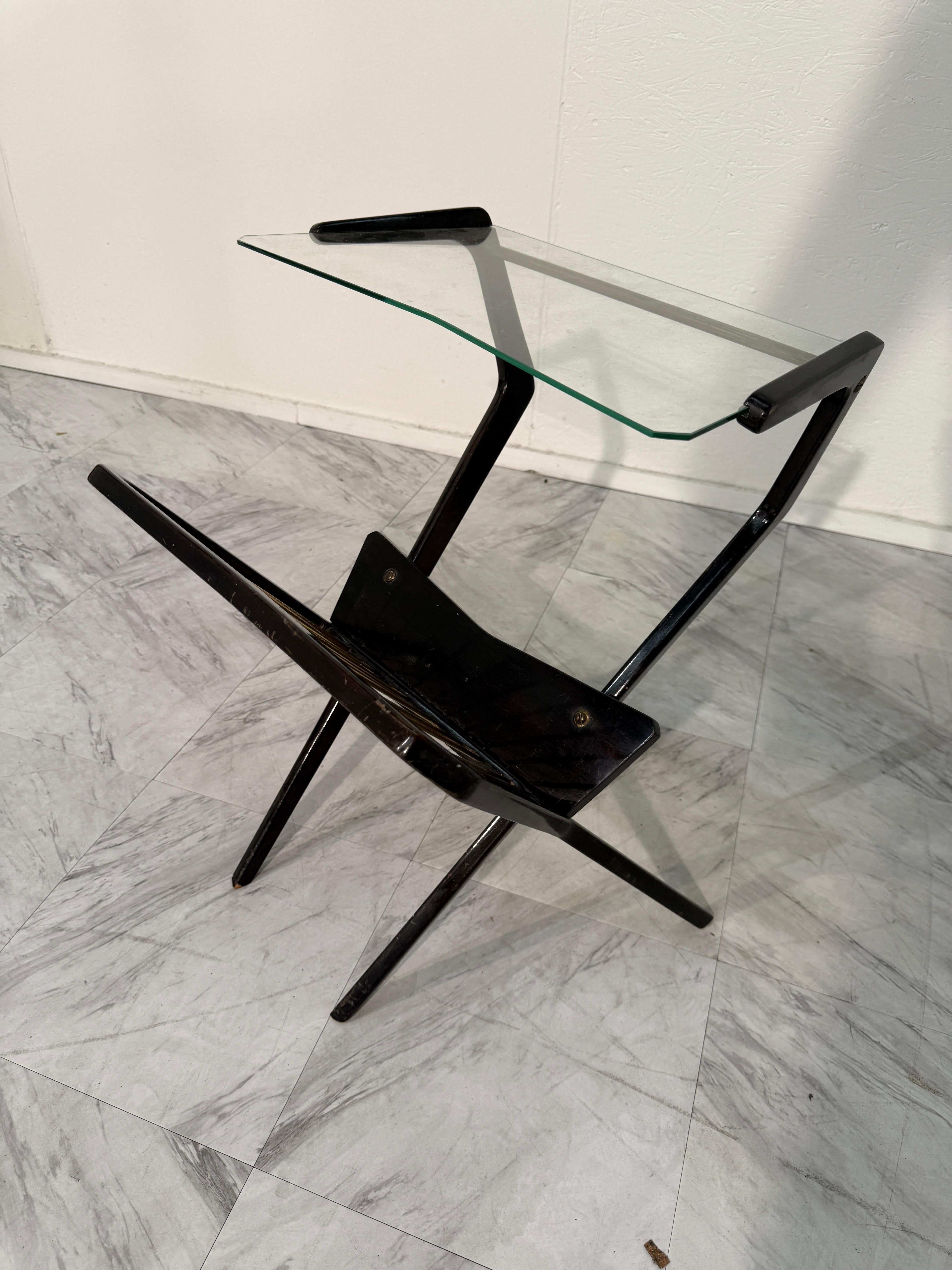 Tavolino portariviste di metà secolo, realizzato in Italia negli anni Cinquanta-Sessanta. Questo pezzo combina un'intelaiatura scultorea in legno con accenti in ottone e un profilo angolare, incarnando le linee audaci del design modernista italiano.