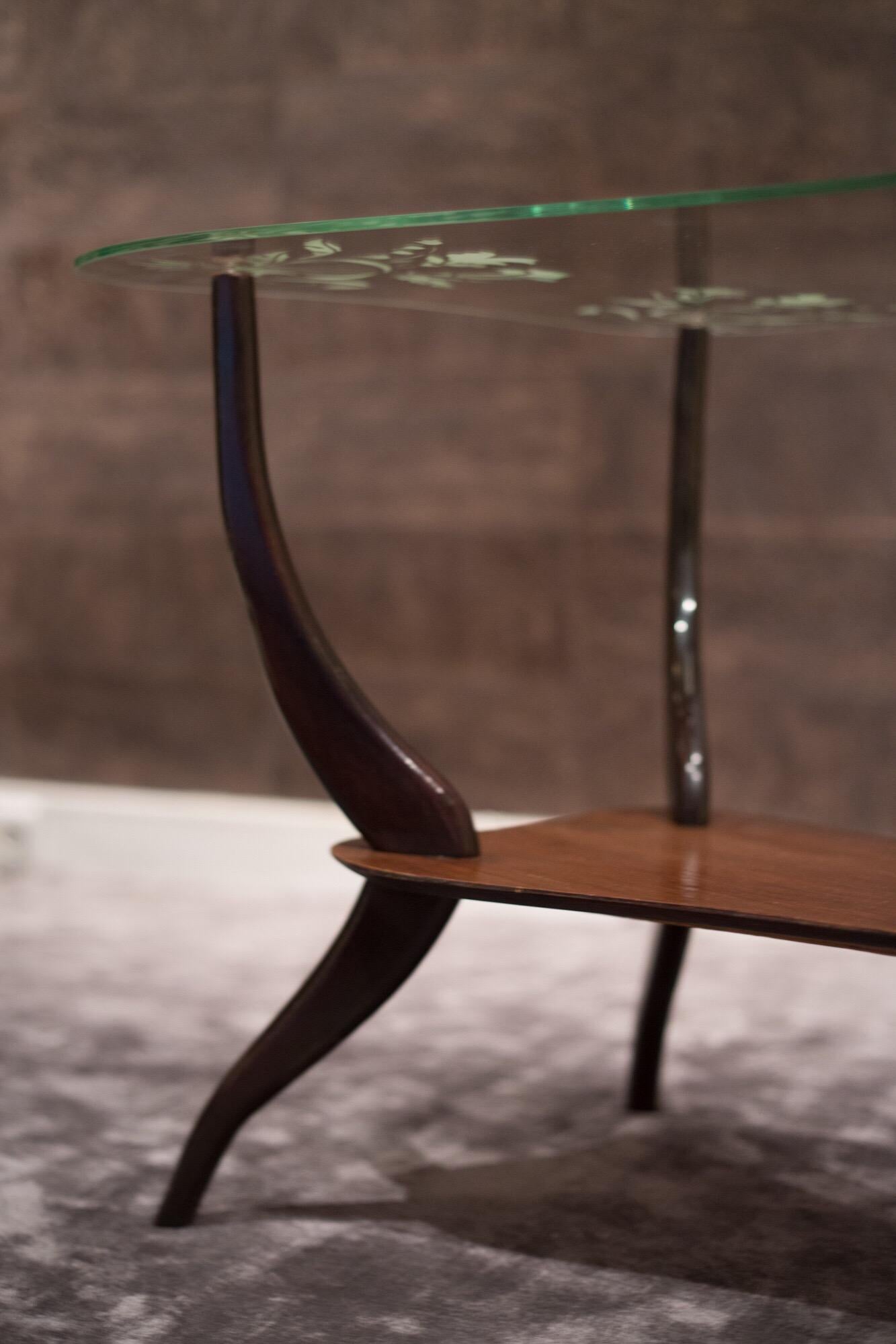 1950s Italian coffee table by Ico Parisi.
This table's top irregular shape was specifically conceived to be able to draw it as close as possible to a sofa or armchair. The tabletop glass is enhanced with a lovely decorative floral pattern.
Supported