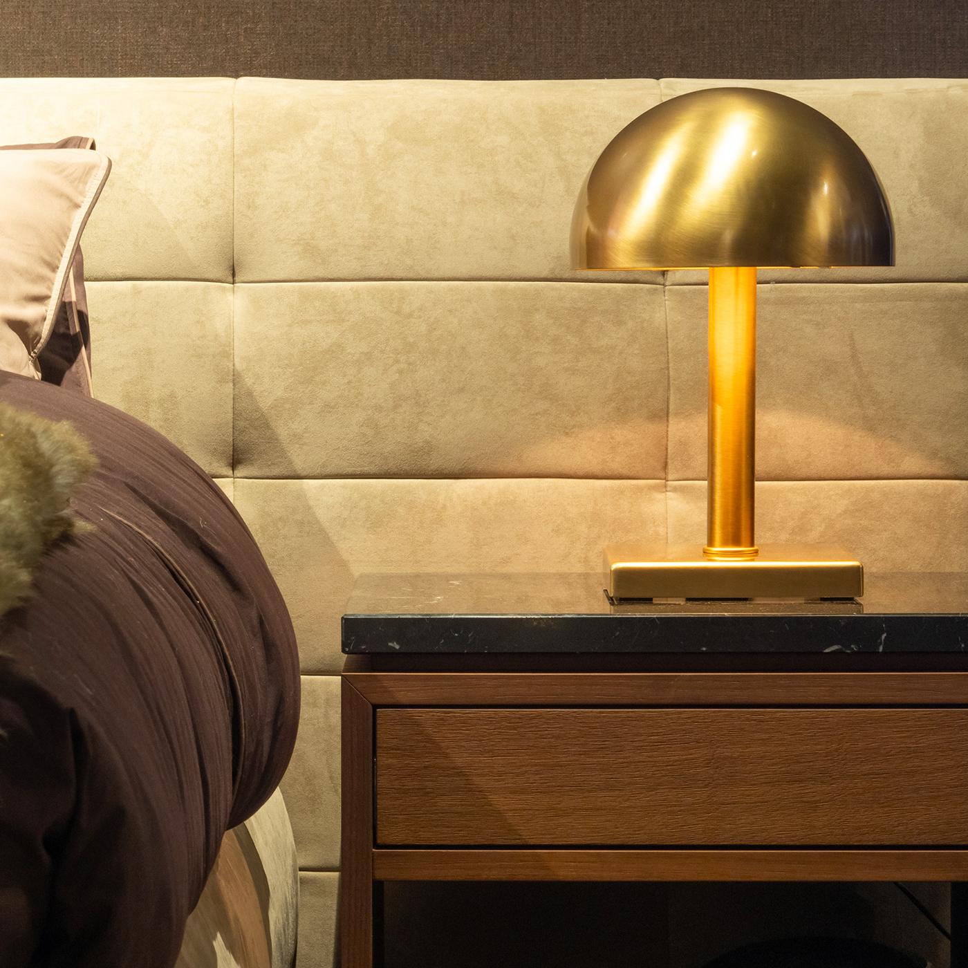 Part of the Blake collection, this table lamp is a stylish combination of pure geometric volumes. Its square base and cylindrical stem support a semi-spherical shade in bronzed brass that creates a diffused ambiance light.