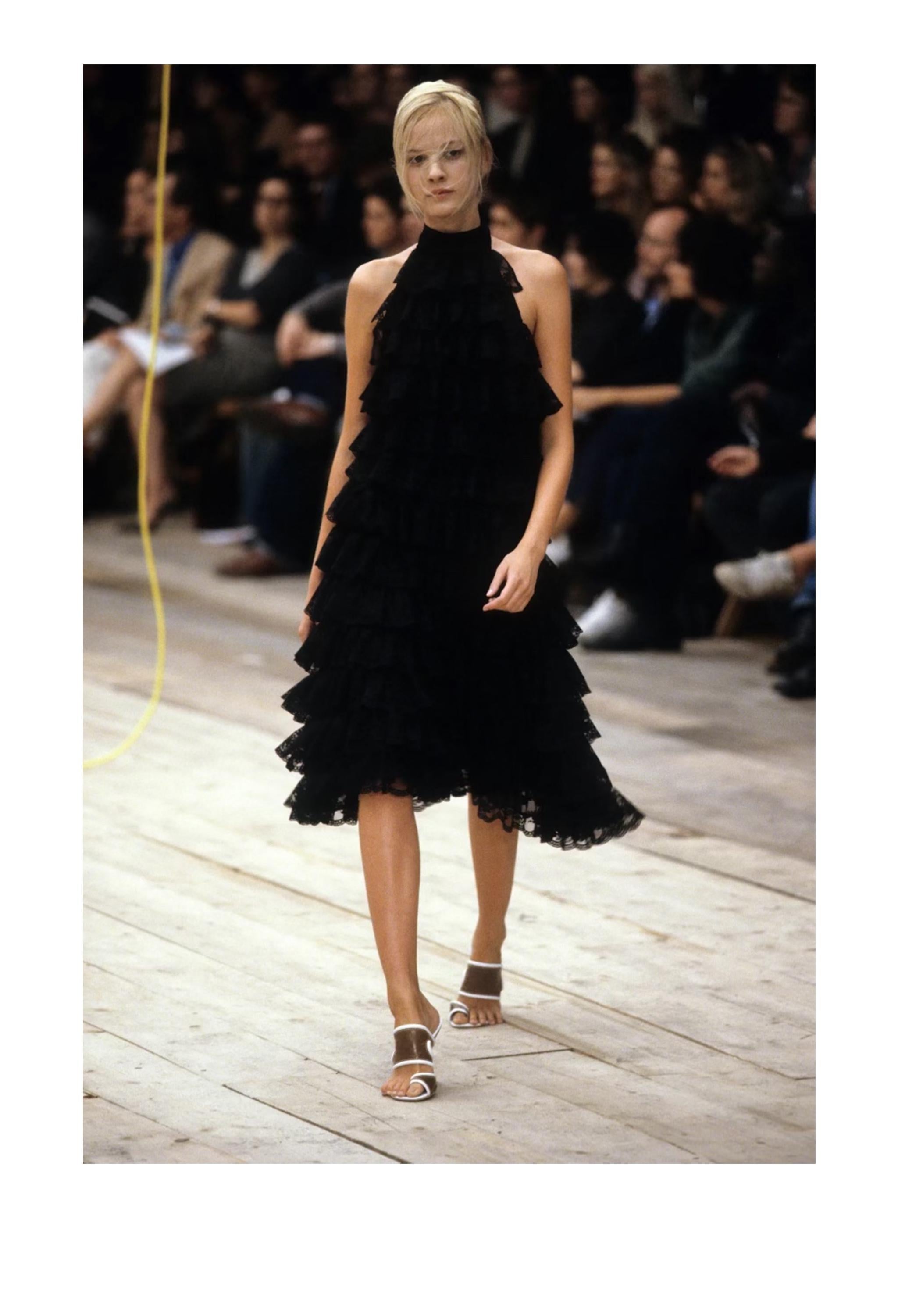 Resurrection Vintage is excited to offer an important Alexander McQueen black cocktail dress from the 1999 runway collection featuring rows of lace ruffles, a high neck with button closure in the back, halter body, exposed sides and open back, and