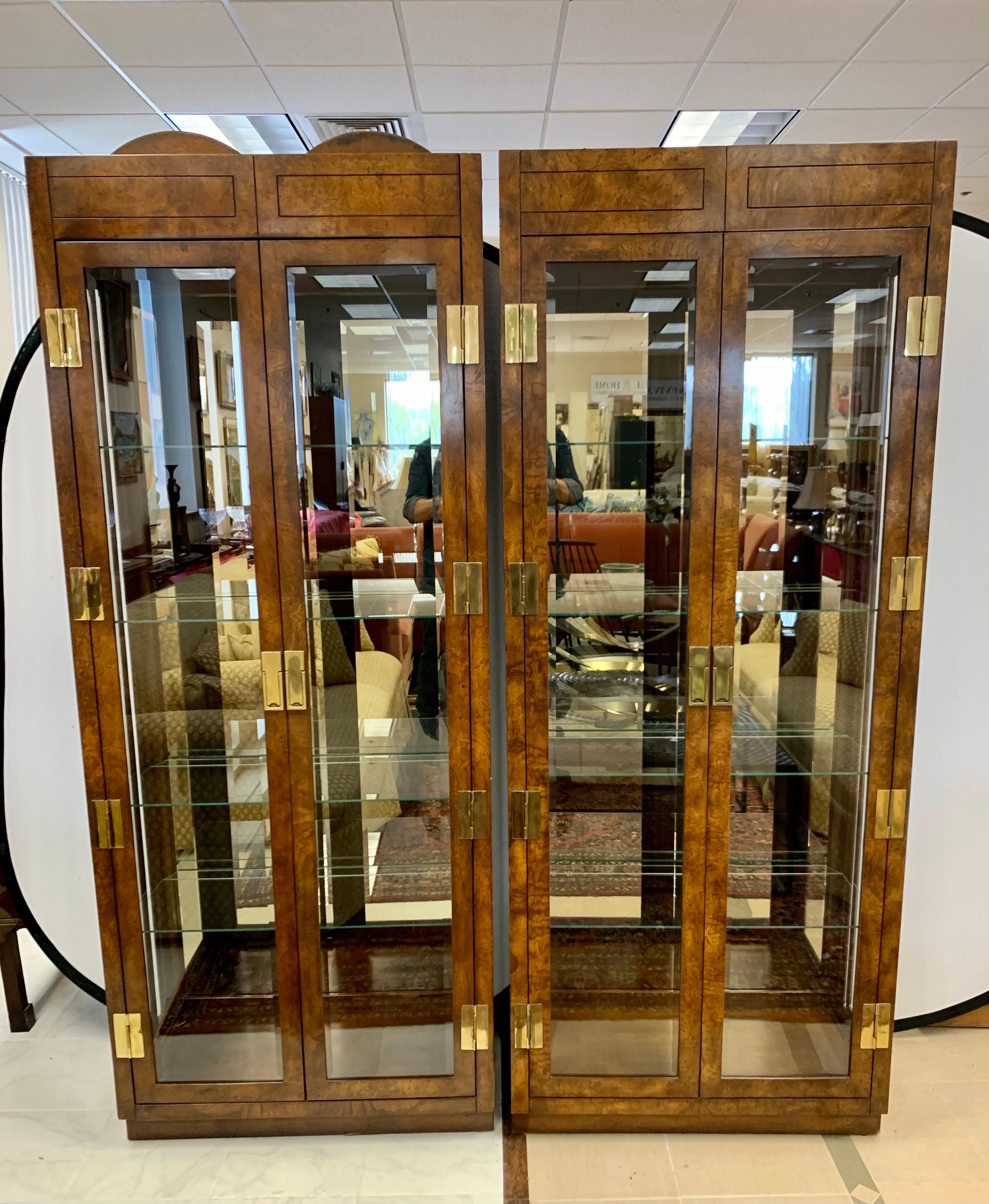 Matching pair of rare and iconic signed mid century burl and glass vitrines from American of Martinsville. Made in the USA, circa 1970's. Come with custom glass shelves and fully electrified. Campaign styling at its best. Features all original brass