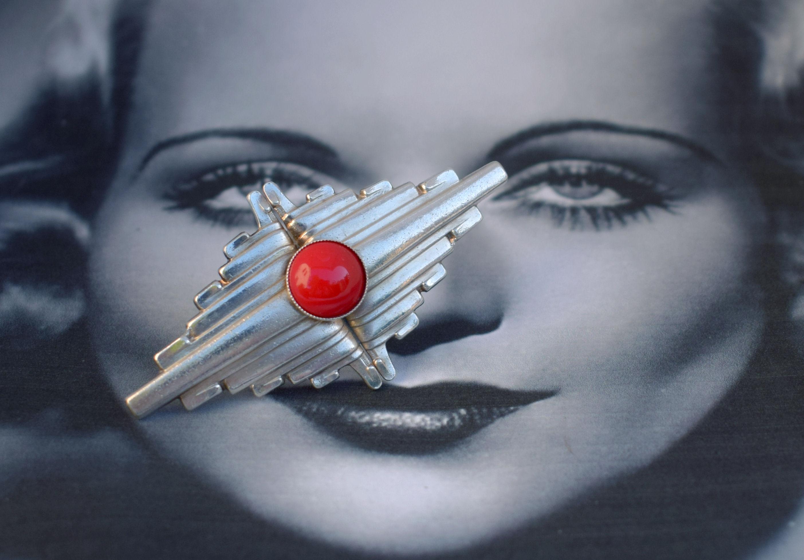 Iconically shaped Art Deco style brooch, beautifully made. The bright red glass center stone against the silvered back ground really makes this piece pop. You can wear this for any occasion, perfect for the black jacket or jumper even a scarf. If