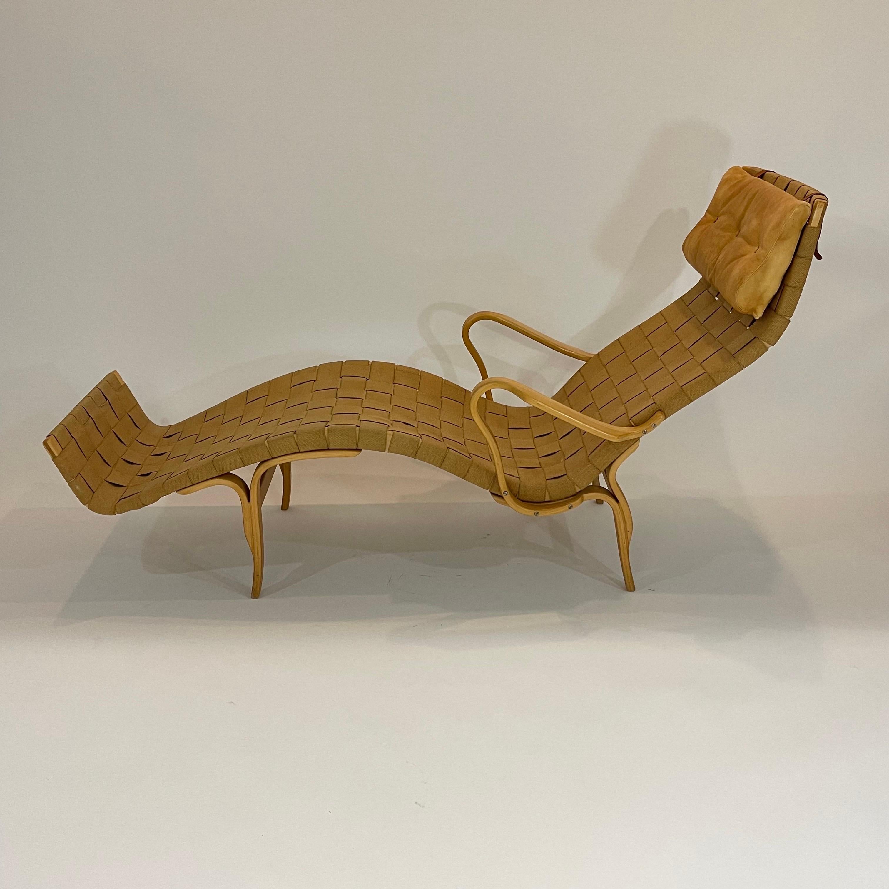 Iconic Original MidCentury Scandinavian Pernilla chaise lounge with arms, rendered in a bent beech wood frame with handwoven hemp burlap webbing strapping and an upholstered natural leather button tufted headrest pillow cushion affixed with saddle
