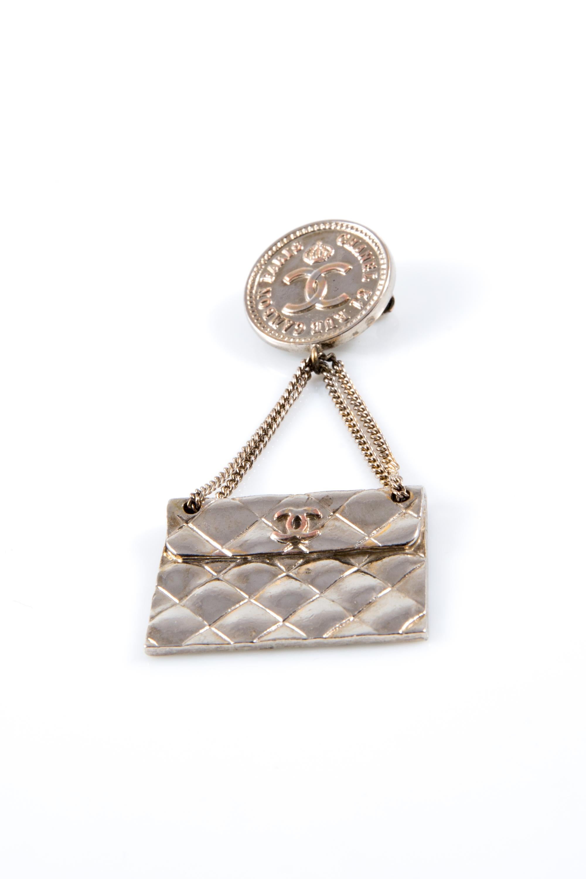 Chanel Silberfarbene CC-Taschen-Brosche mit einer freien gesteppten Tasche, einer silberfarbenen Kette und einer runden Chanel-Logo-Münze oben, einem Verschluss mit Nadel hinten und einer angefressenen Plakette hinten. Um die 2000er Jahre.
Guter