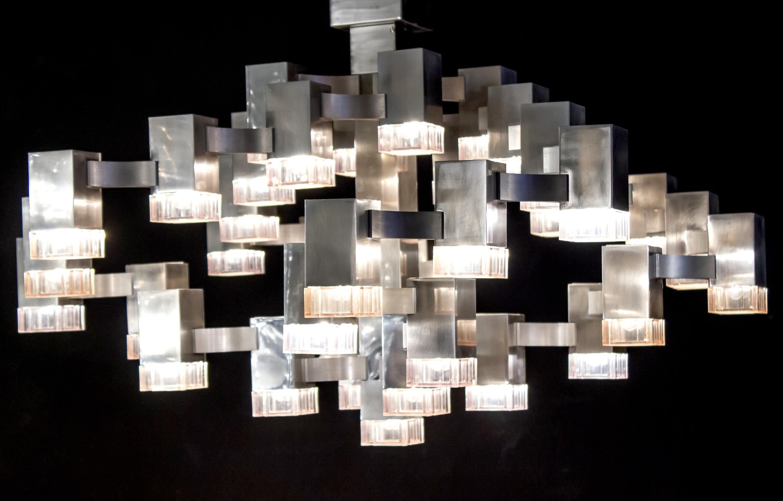 Famous chandelier belonging to the series inspired by a trip of Gaetano Sciolari in New York, the chandelier is composed of 37 lights that radiate a striking light.
Structure is made of chromed brass cubes connected together with aluminium bridge