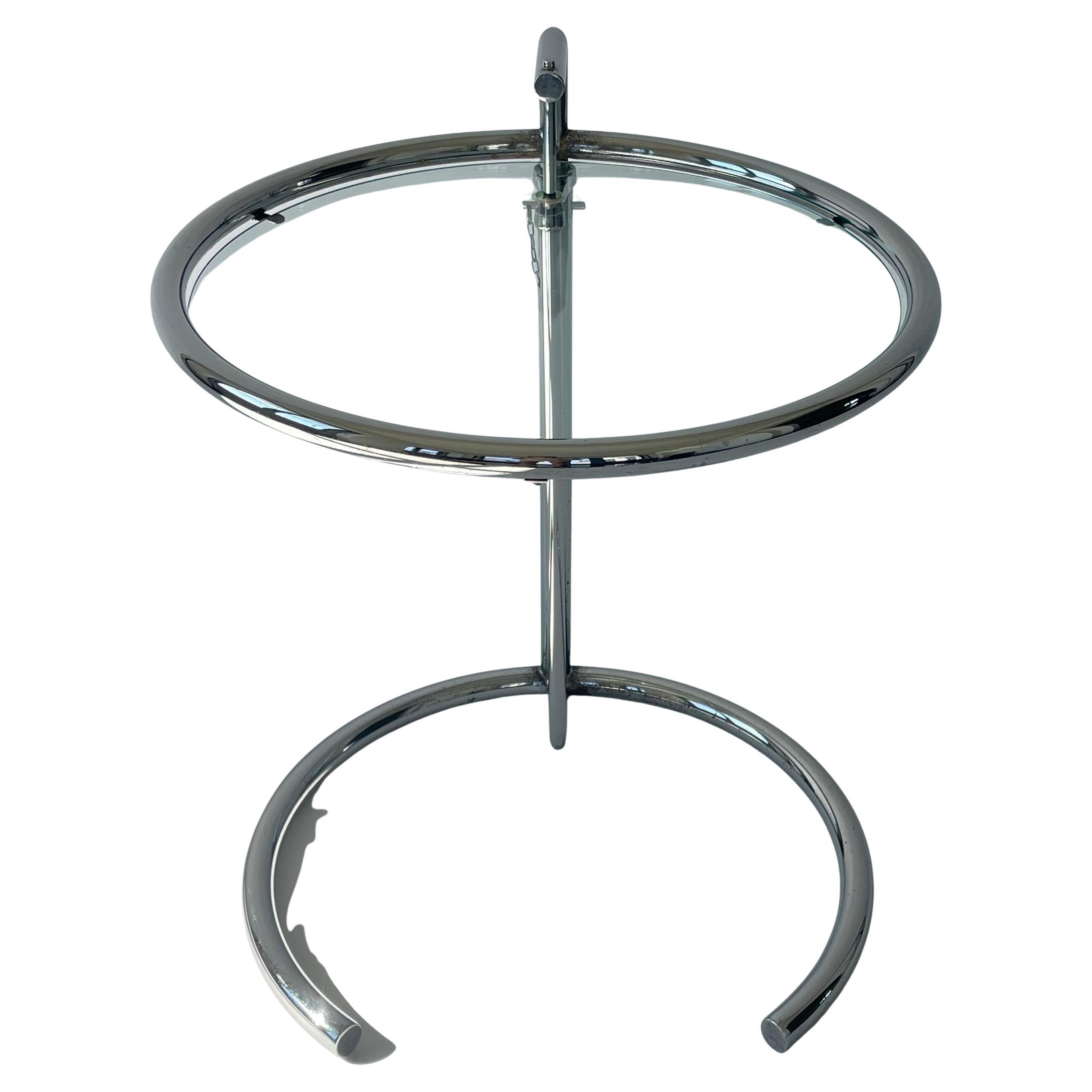 Table réglable Iconic E 1027 en acier chromé avec plateau en verre.  La table est réglable en hauteur tous les deux pouces et s'étend jusqu'à 38,5 pouces de haut.  Le plateau de la table en verre est 3