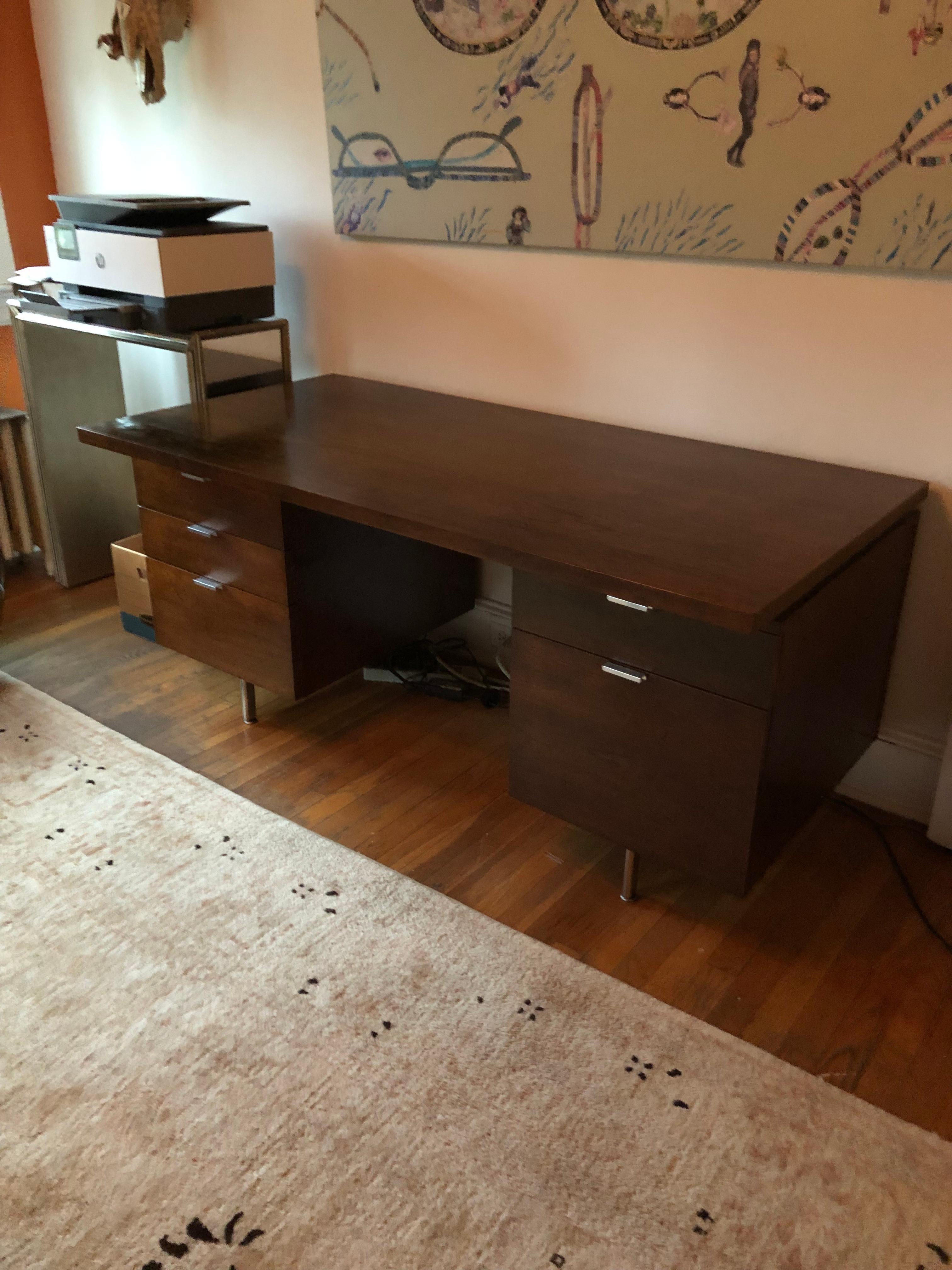 Executive desk with the George Nelson label inside the top right drawer having Mid-Century Modern Classic design and streamlined function with floating wood top on two sides of drawers, raised up on simple cylindrical steel feet. Timeless sleek