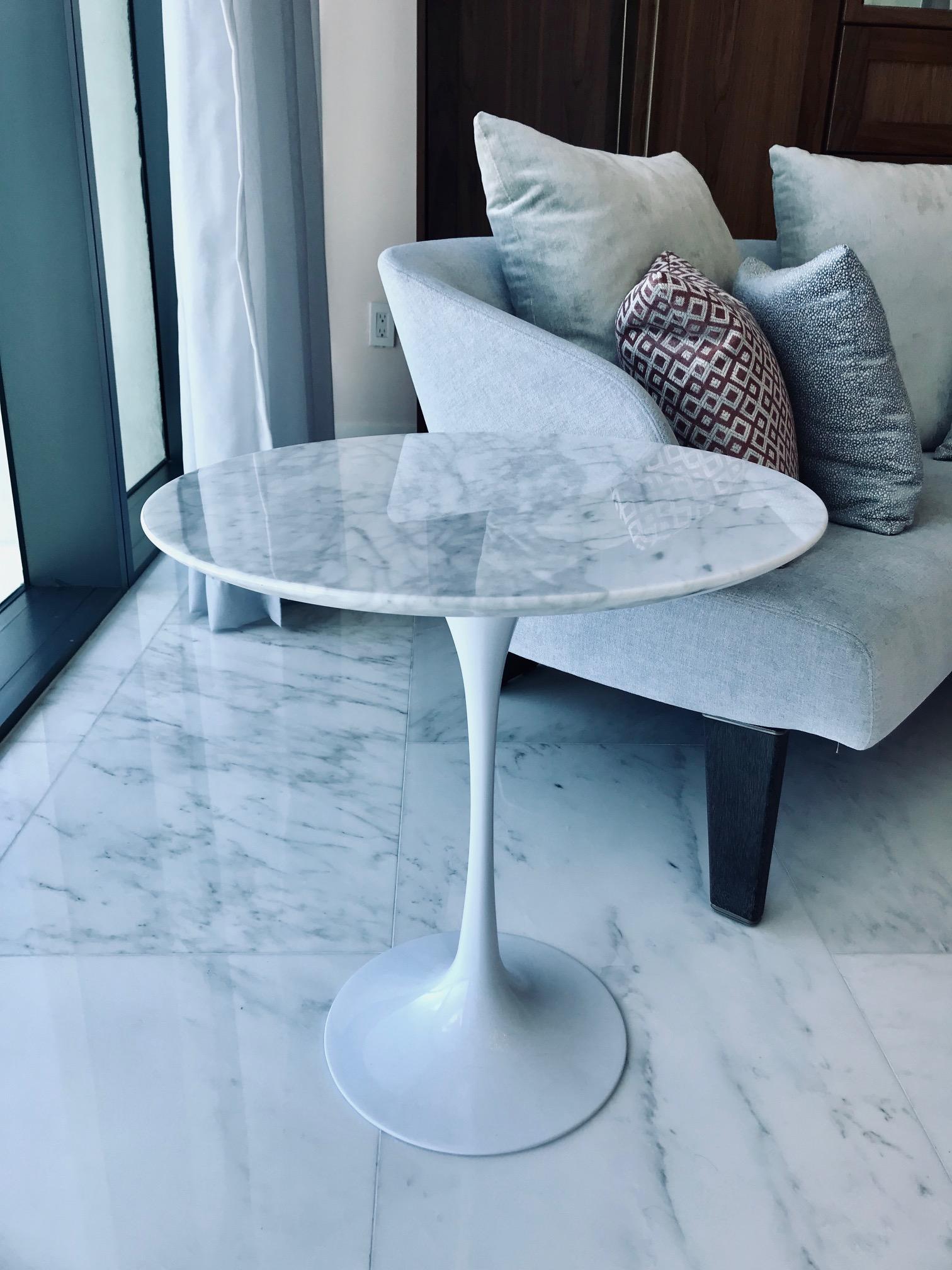 The iconic tulip side table comprised of solid arabescato Carrara marble top over a stylized cast metal base in a white gloss enamel finish. Originally designed by Eero Saarinen in the late 1950s. Fitted with round polished white marble top with