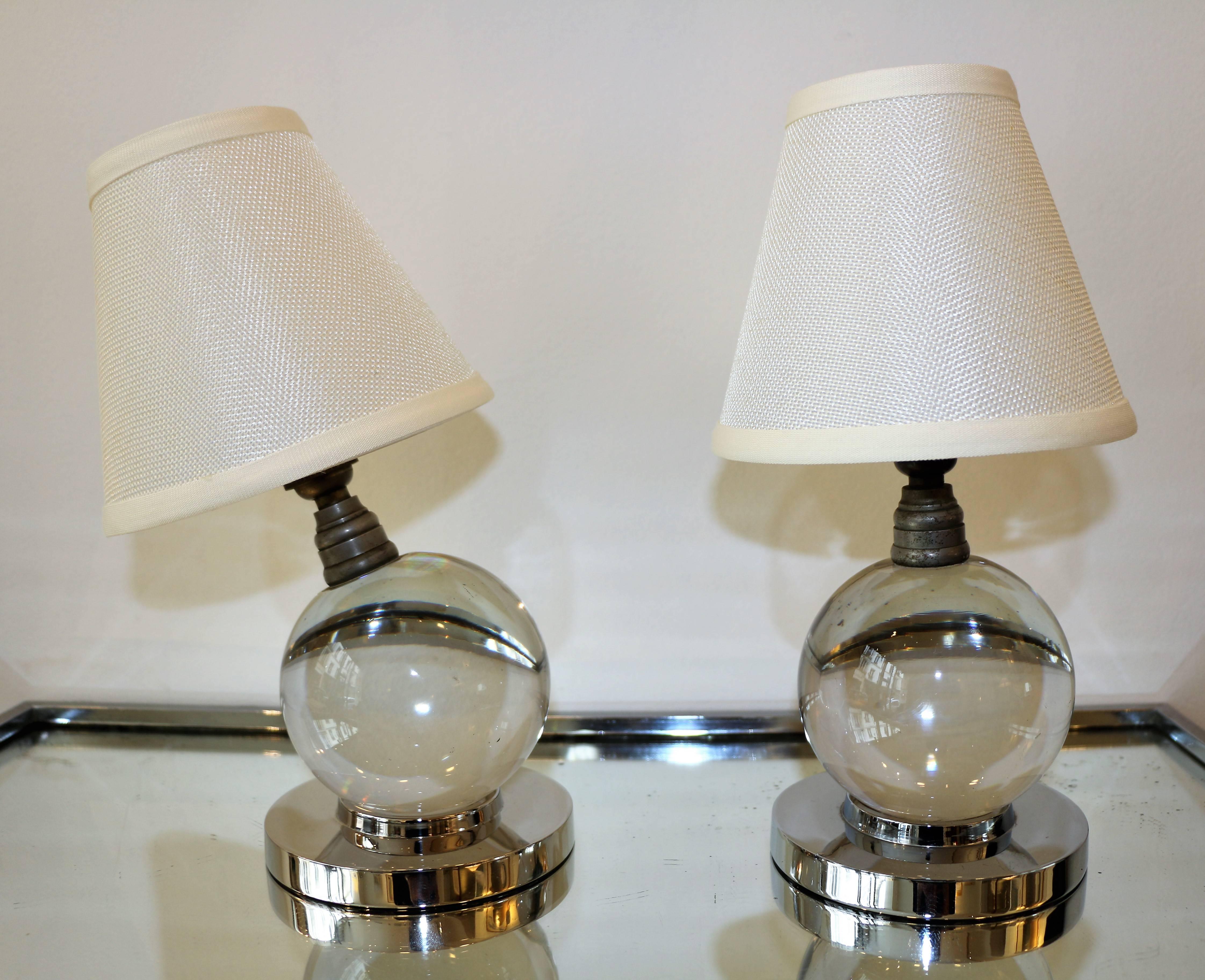 This pair of table lamps by Jacques Adnet & Baccarat is an icon of the modernist Art Deco style. Each lamp is made of a solid globe of glass simply lying on a chromium plated metal base. It can be put in any position. The shades are new. Wired for