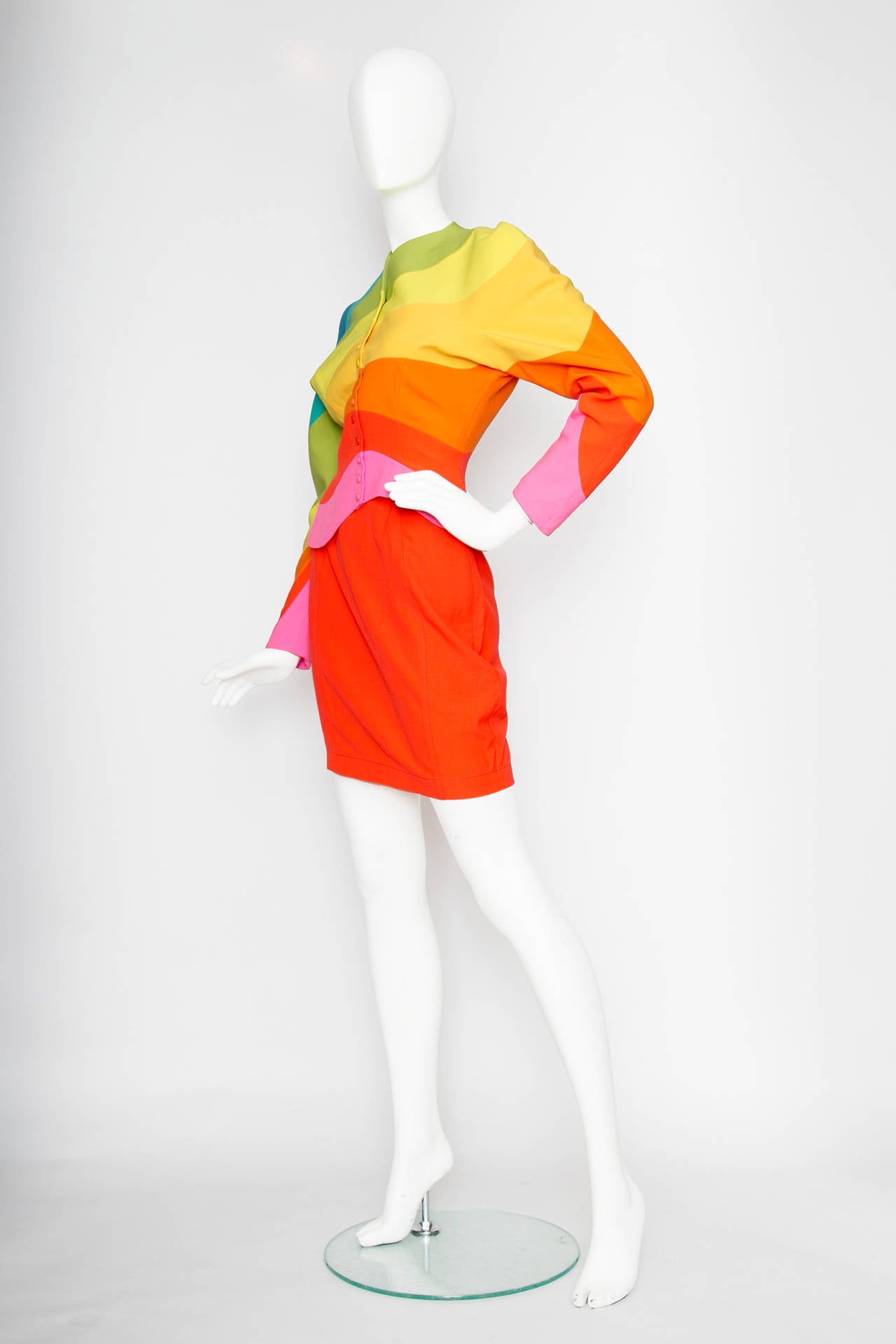 An increddible 1990s Thierry Mugler wool skirt suit with a fitted jacket with abstract pattern in an array of bright colours. The jacket has rounded edges and an asymmetrical hemline, tapered sleeves and a pushbutton closure. The buttons vary in