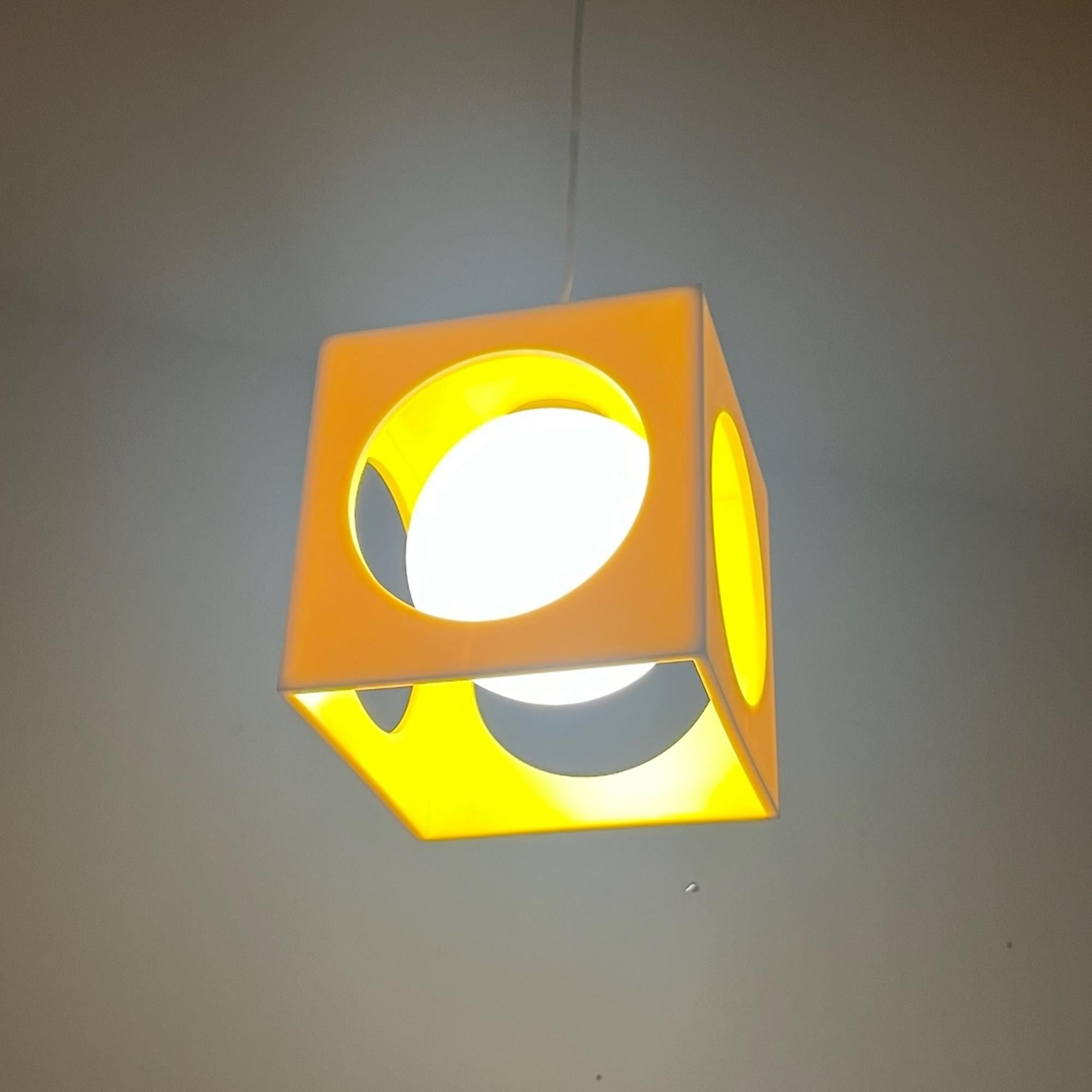 Illuminate your space with this striking space age lamp designed by Richard Essig Besigheim. This unique hanging lamp features a glossy yellow plastic cube with rounded holes, perfectly housing a sphere of opaline white glass. The combination of