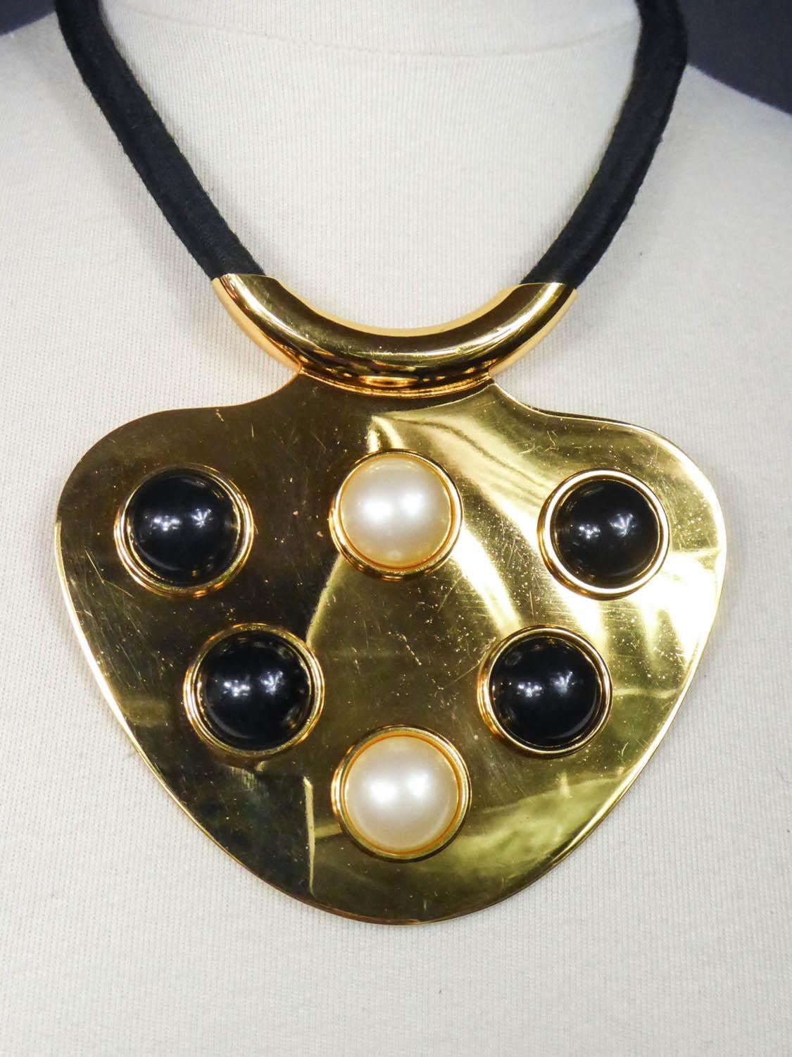 Circa 1970
Paris France

Imposing and iconic pendant necklace by Lanvin from the early 1970s of the Space Age period. Large crew-neck medallion in shiny golden brass in the shape of drop. Cabochons of large half beads in black and pearly bakelite,