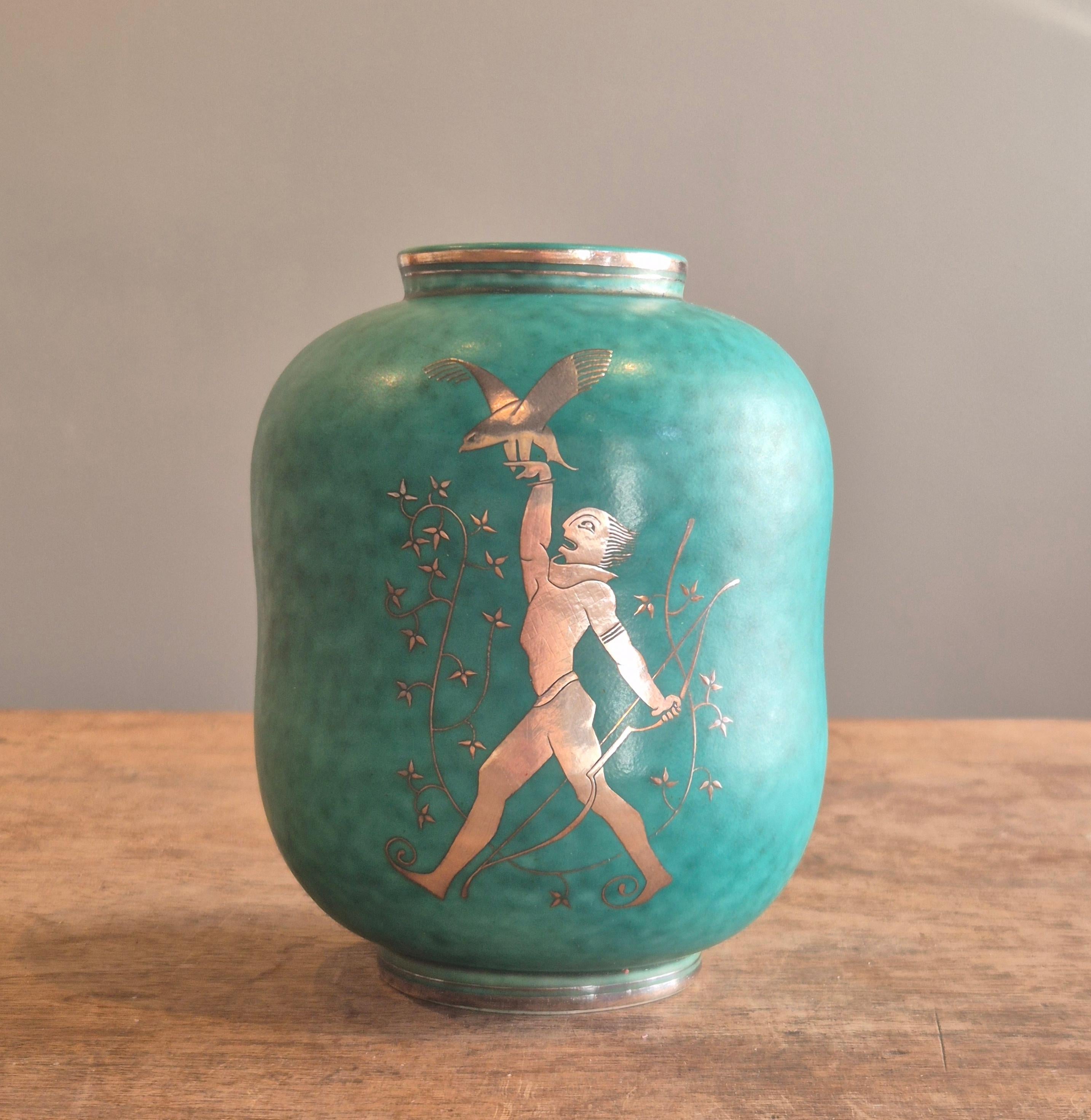 Ein schwedischer Klassiker der Moderne, Vase aus Steinzeug in grüner Glasur mit Dekor einer mythischen Figur/eines Jägers mit Falke und silbernen Streifen am Rand. Entworfen von Wilhelm Kåge aus der Serie 'Argenta' für Gustavsberg,