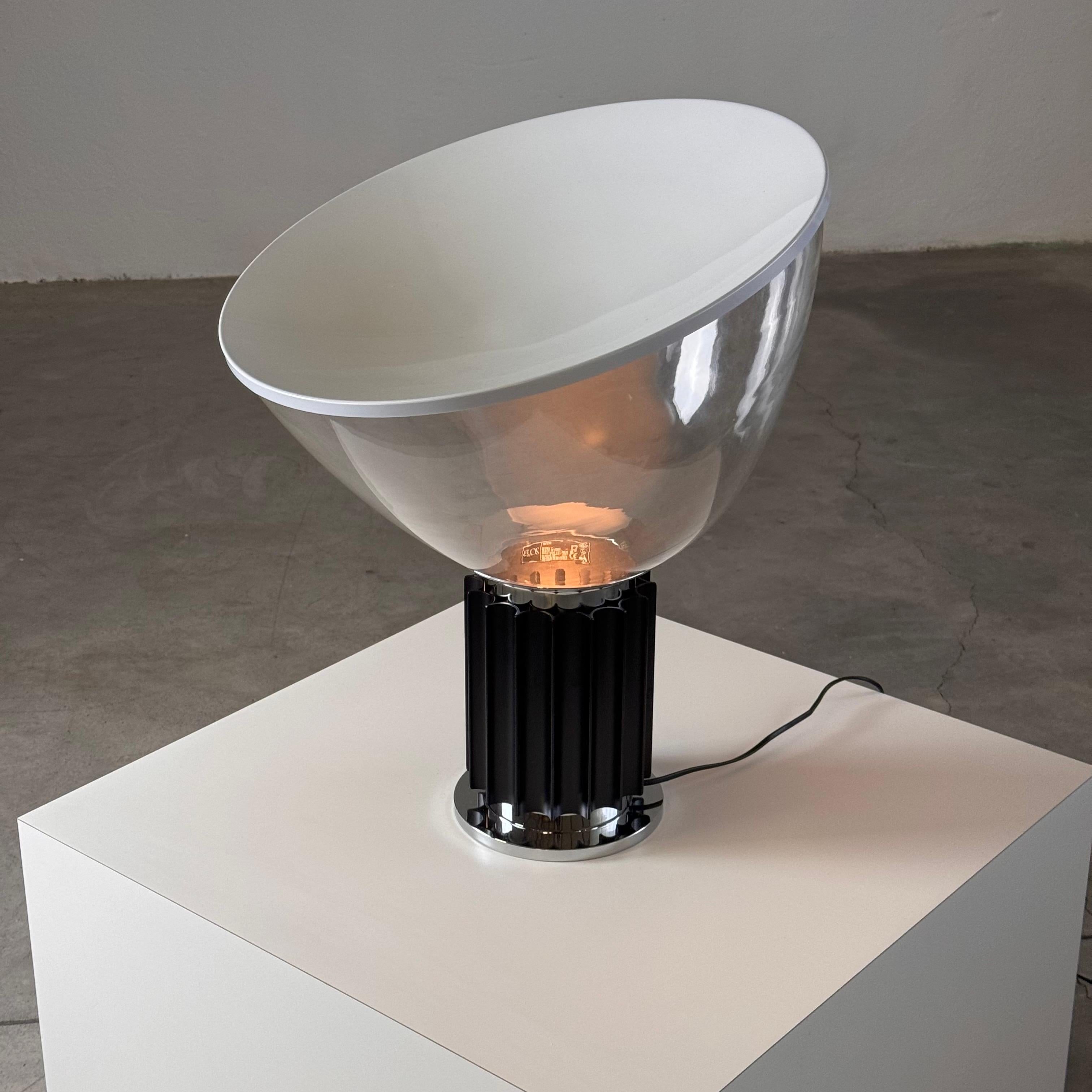 Un pezzo iconico del design italiano, questa lampada da tavolo Taccia di Achille e Pier Giacomo Castiglioni per Flos. È stata esposta delicatamente solo in una vetrina per un breve periodo, preservando le sue condizioni incontaminate con l'etichetta
