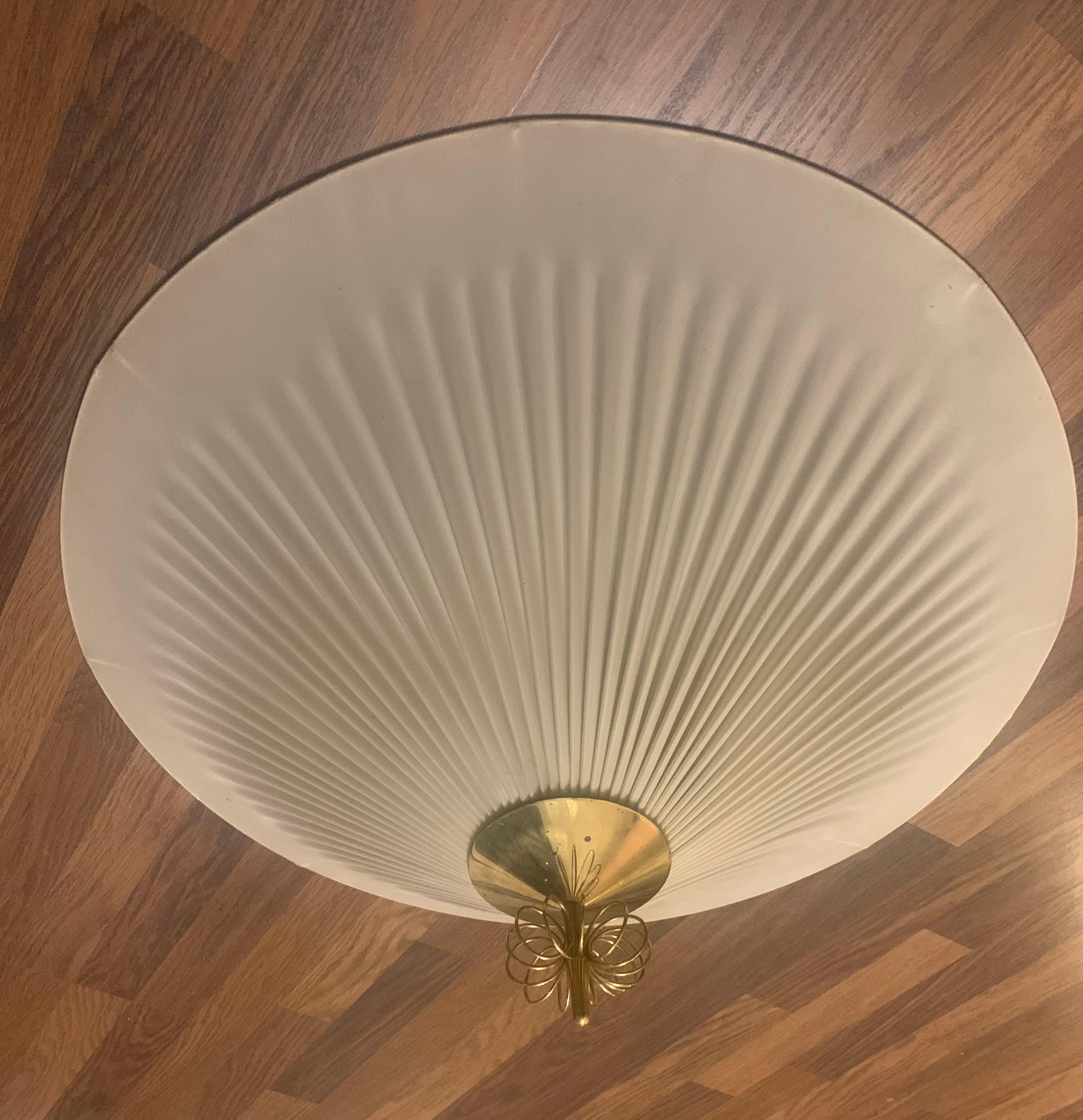 Voici la traduction :

---

Le modèle 1076 d'Idman Plafondi, conçu au début des années 1950, est un exemple étonnant du design finlandais du milieu du siècle dernier. La lampe se compose de laiton poli et d'un abat-jour en plastique moulé avec trois