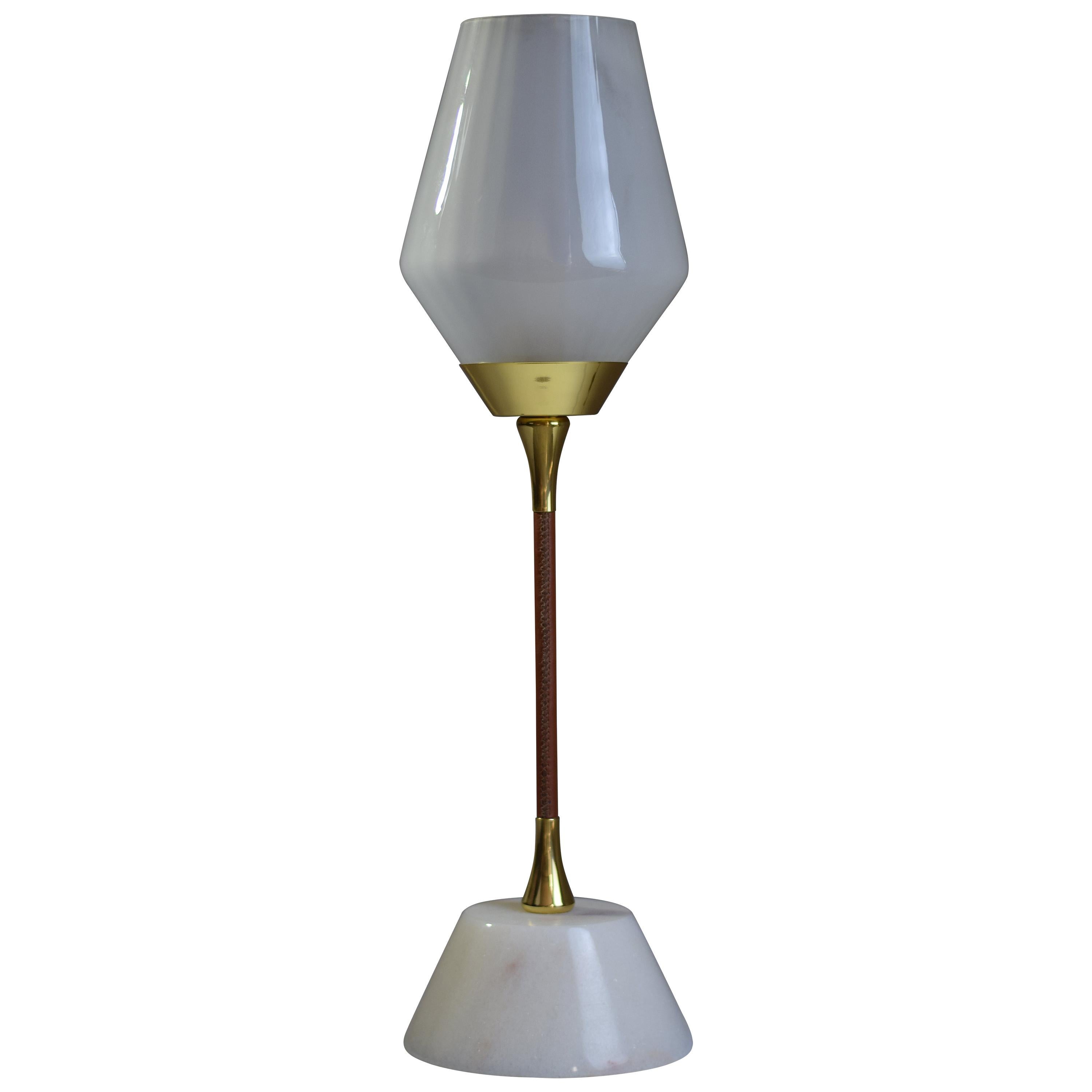 A table lamp composed of a leather sheathed brass stand. The base is carved out of Carrara marble. The glass shade reflects the light upwards and the opal di uses the light around the room.
1x60 W Max E14
230 V - LED Integrated 120 V -
