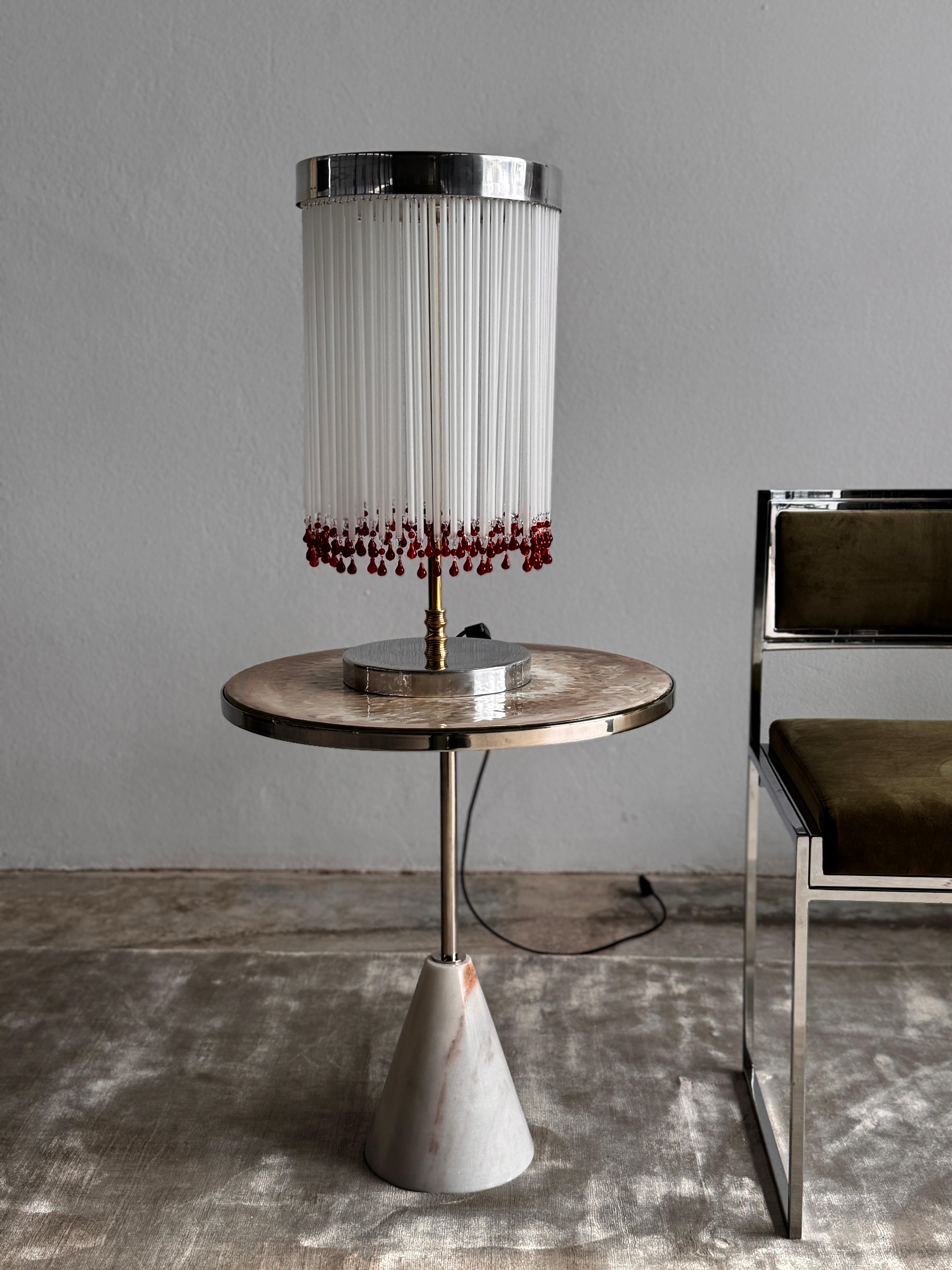 Fabricada a mano en Portugal, la IDRIA T2-NW presenta una cortina cilíndrica de varillas de cristal blanco esmerilado, cada una de las cuales termina con una gota de cristal rojo rubí delicadamente aplicada a mano. Esta sorprendente combinación de