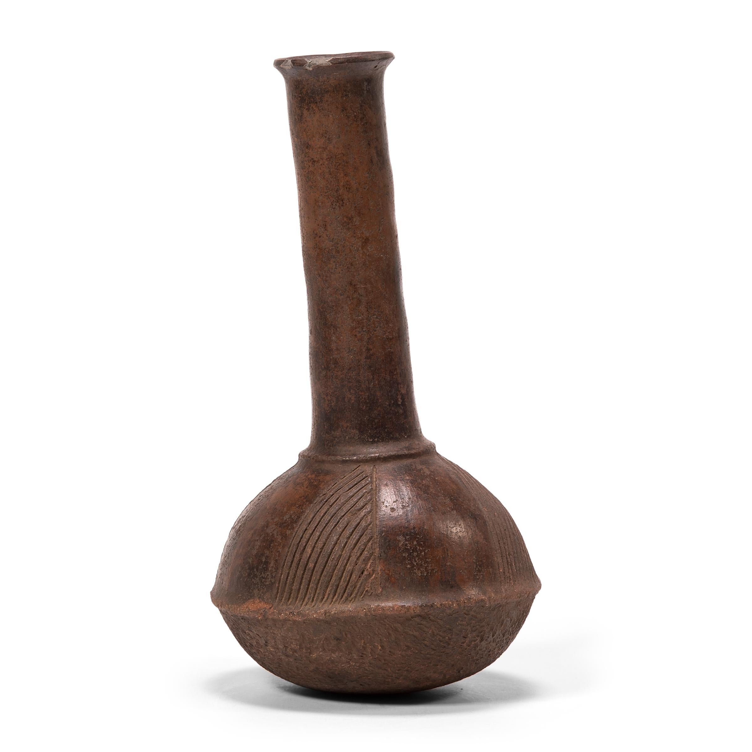 This tall, bottle-necked vase was created by an artisan of the Igbo People of Nigeria. Bottle forms, once common in pre-historic West African ceramics, are rare in the historic record. An elongated neck meets the oblong body with a slight ridge,