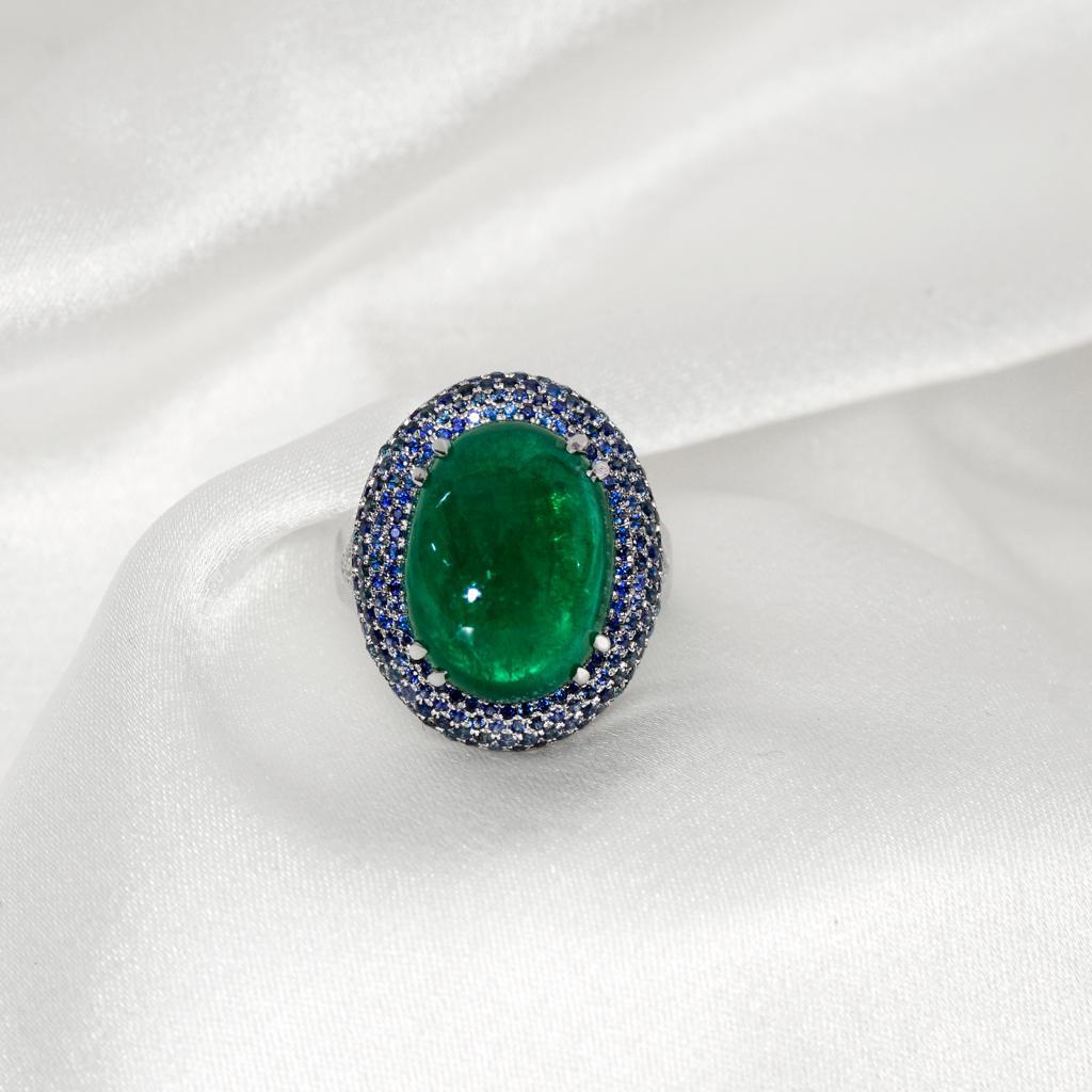 Beautiful 14 Karat white gold cocktail ring with a natural 13.56 ct great quality green Emerald as center stone surrounding natural sapphires weighing 1.51 ct and natural diamonds weighing 0.22 ct. This ring combines classical with modern elements