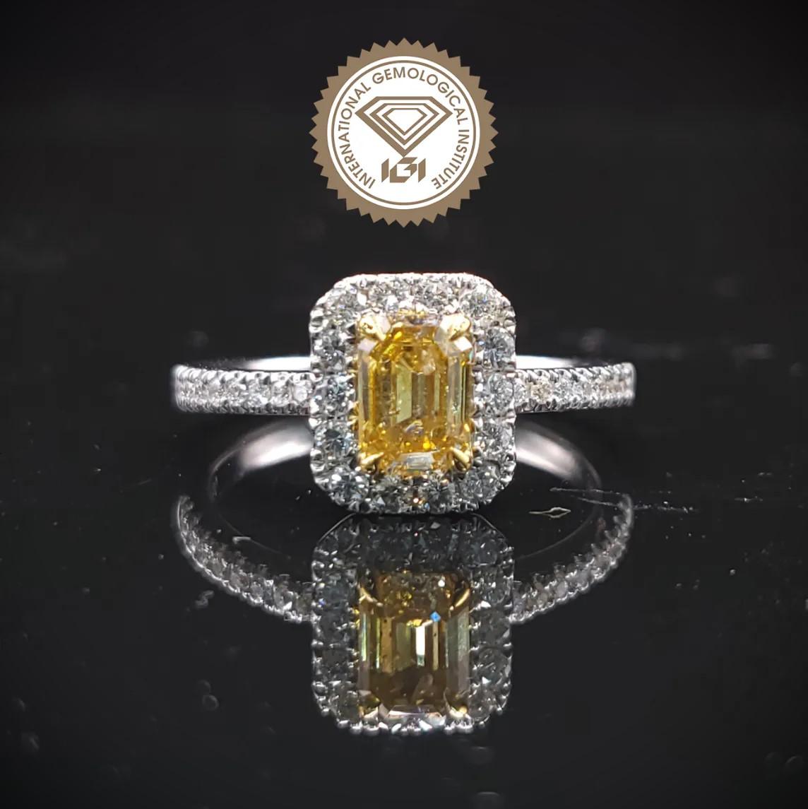This exquisite ring showcases a captivating 0.59-carat emerald-cut Fancy Intense Orangy Yellow diamond as its centerpiece. The diamond, with its warm, unique color, is set in a classic four-prong setting, allowing its brilliance and character to