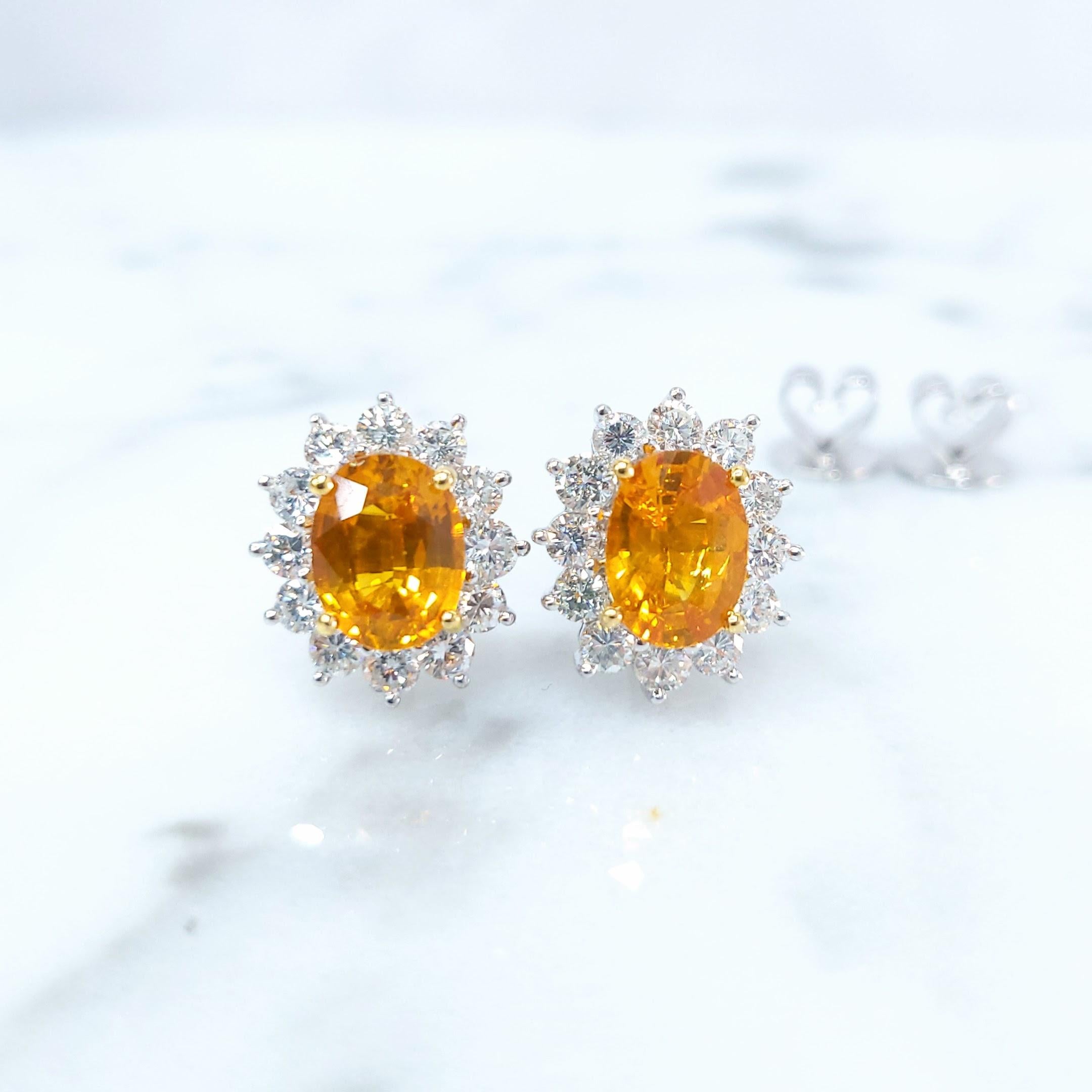 Deslumbrantes pendientes de oro amarillo y blanco de 18k con vibrantes zafiros naranjas y brillantes diamantes. Estos exquisitos pendientes presentan dos zafiros naranjas naturales ovalados de talla mixta, cada uno con un intenso tono naranja que