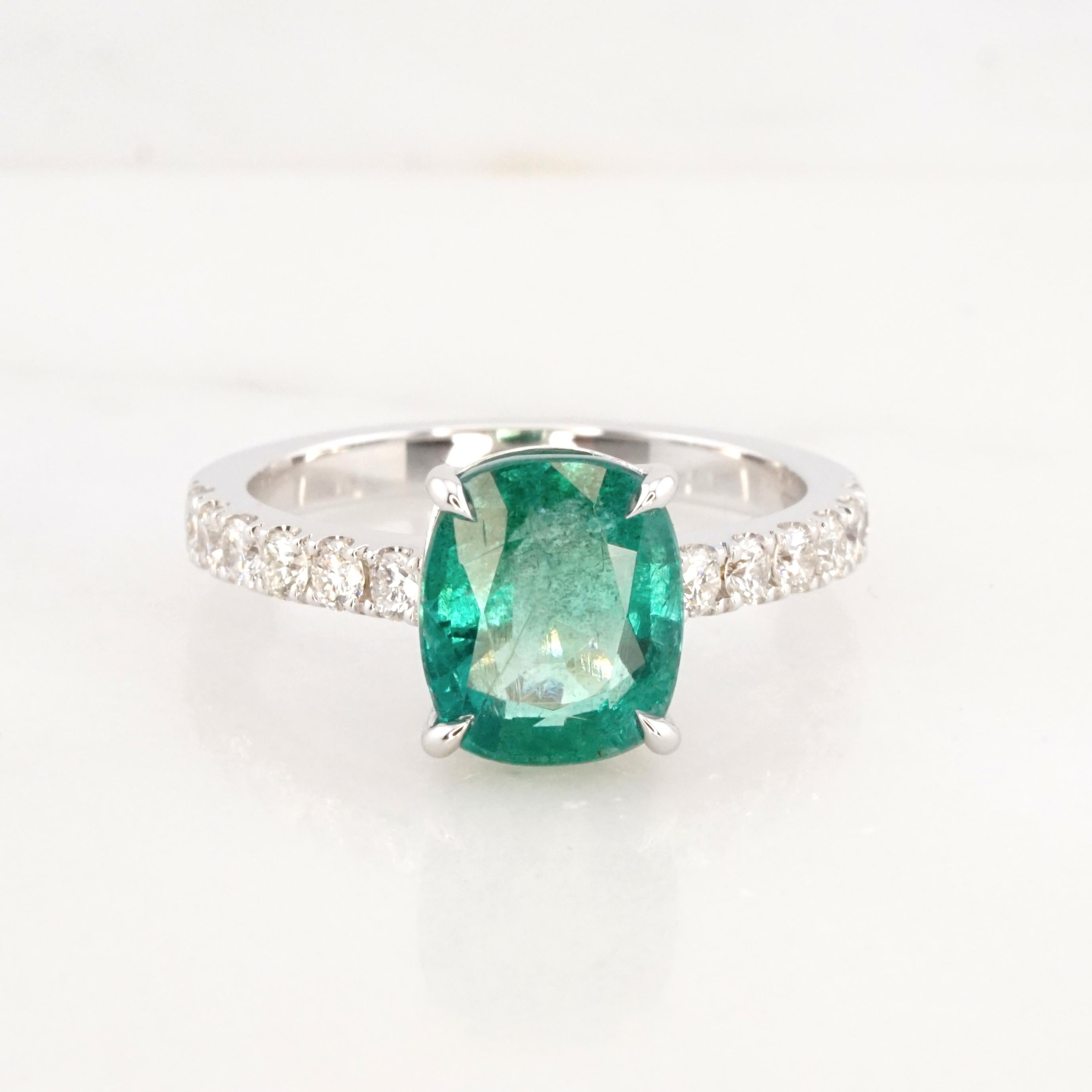 This exquisite cushion-cut emerald ring is a masterpiece of elegance and sophistication. At its heart lies a mesmerizing IGI Certified 3-carat natural emerald, boasting a vibrant, translucent green that captures the very essence of nature's