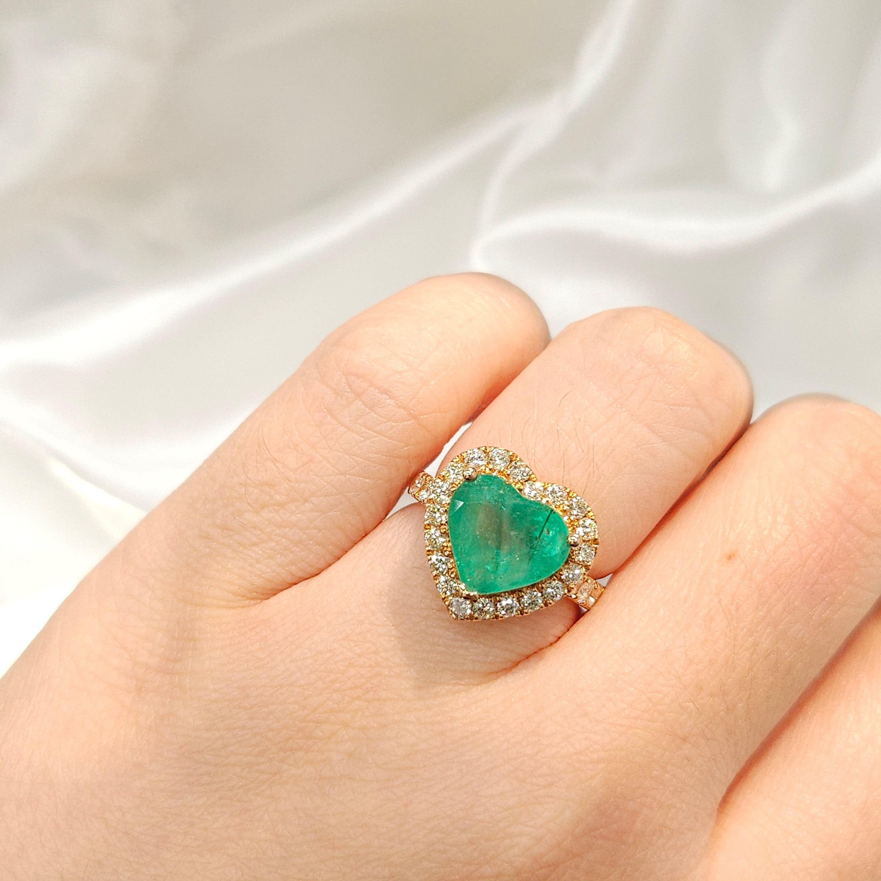 Dive into a world of unparalleled beauty with this enchanting halo ring, featuring a mesmerizing IGI Certified 3.30 Carat Brazilian Emerald that radiates an intense bluish-green hue and takes on the alluring form of a heart shape. The vivid color