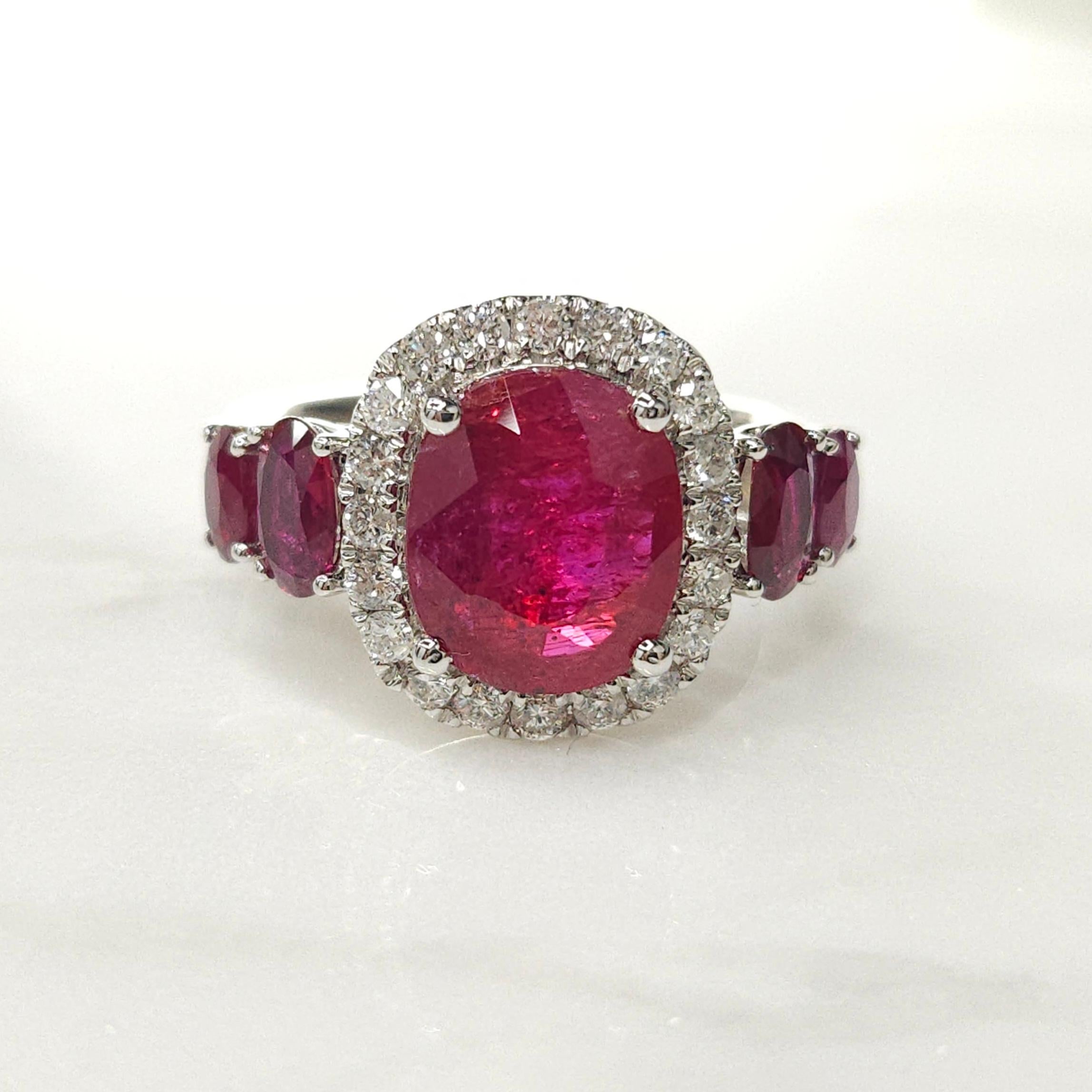 Indulge in the luxurious allure of this captivating halo style ring featuring a dazzling IGI Certified 2.86 Carat ruby in an intense orangy purplish-red hue, meticulously shaped into an elegant oval form that exudes timeless charm and