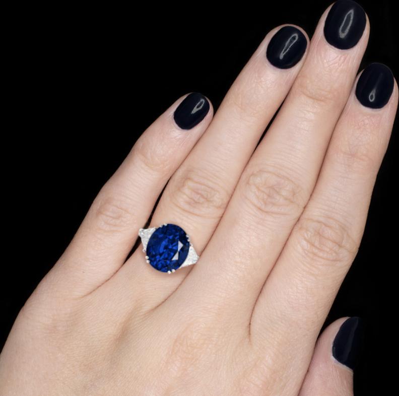 Bague de fiançailles absolument exquise présentant un saphir ovale bleu royal serti dans une monture ouverte à quatre griffes pesant un total de 5 carats.

La pierre centrale est accompagnée de deux diamants de forme trillion de part et d'autre, qui