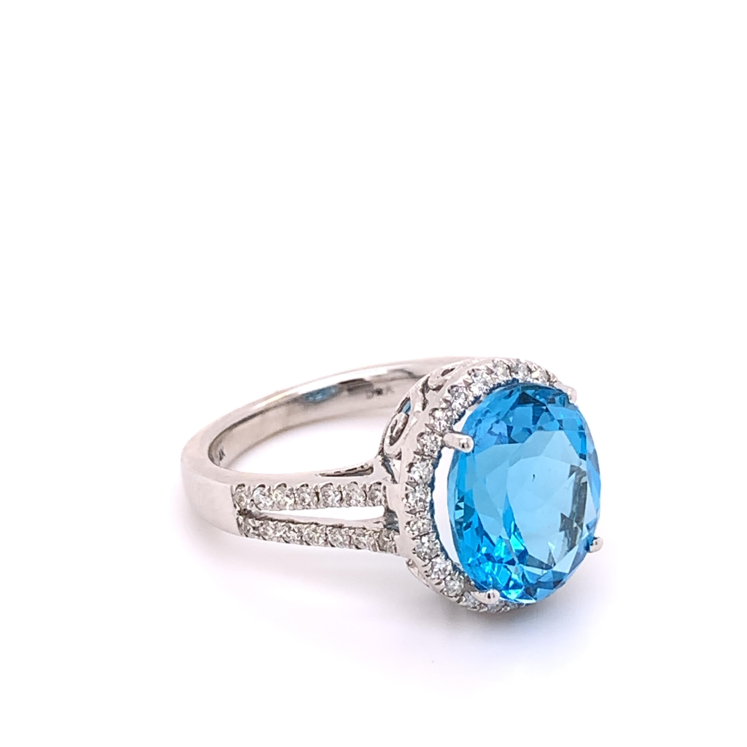 A beautiful ring crafted in luxurious 14 karat white gold with a natural 5.37 carat Blue Topaz stone measuring 11.80 x 9.75 x 6.30mm. This stone is transparent.

This ring also has a shimmering halo and a split shank set with 54 natural round