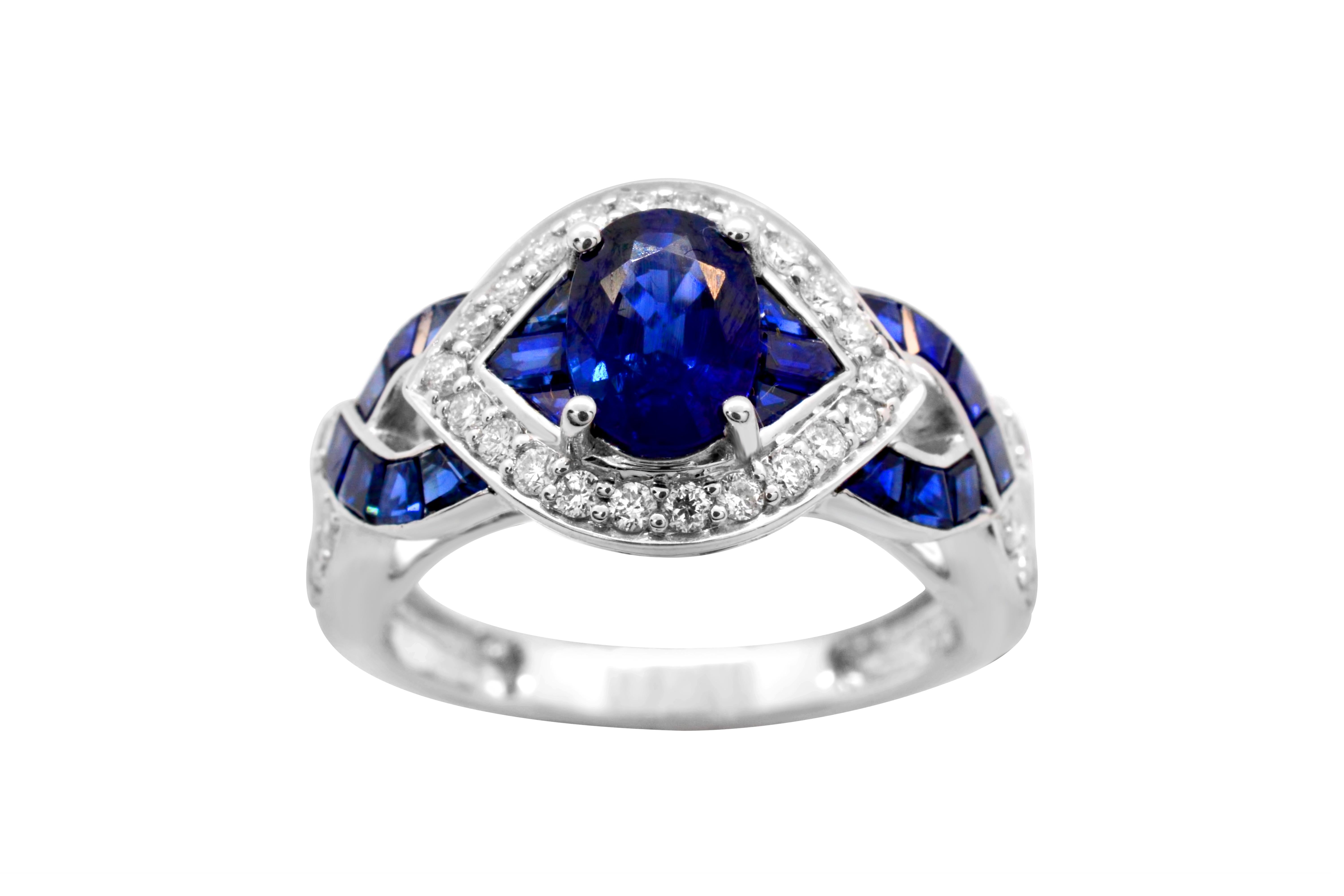Oval Blue Sapphire with Diamond and Openwork Criss Cross Ring.  This ring has an oval blue sapphire measuring 7 x 5 mm at the center.  There are additional blue sapphire baguettes of varying sizes on either side of the center oval as well as the