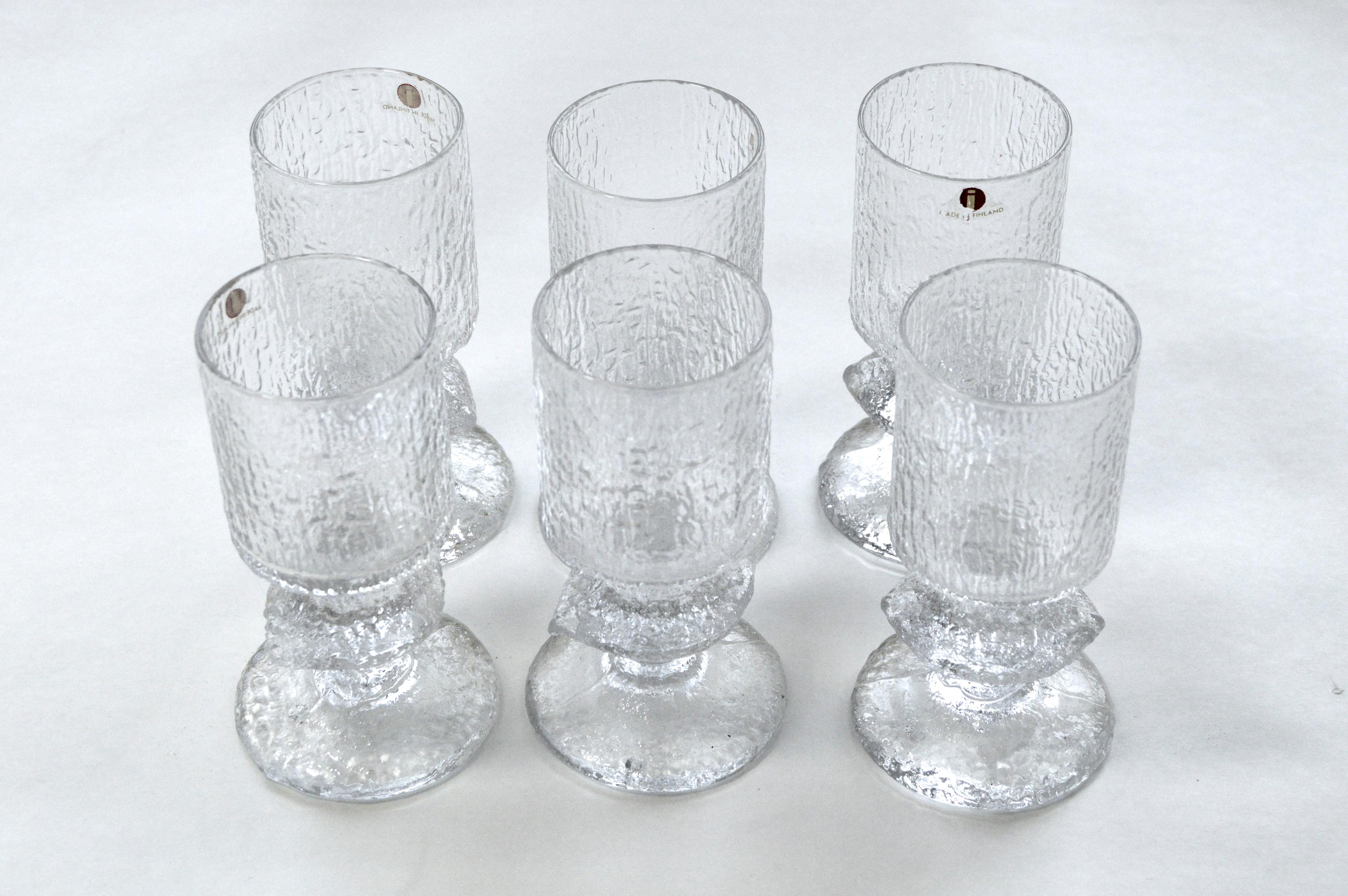 Set of glassware comprised of six large wineglasses, six small aperitif glasses, and two candlesticks. The matching pieces have a rough surface, giving the glass an ice-like texture. Produced since 1967, this glassware has become an icon of Finnish
