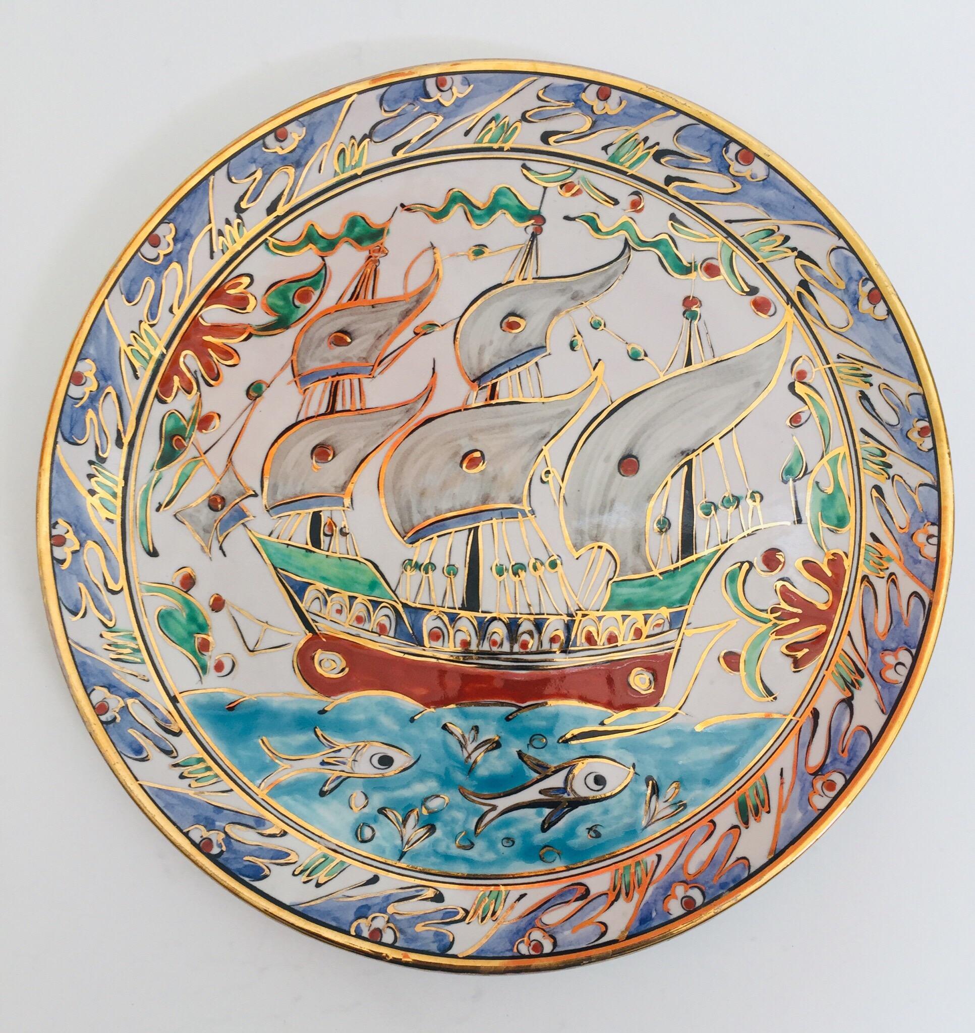 A decorative I Karos Pottery, I Caro collector polychrome hand painted and handcrafted in Rhodes, Greece ceramic wall decorative plate with a boat in the sea and Fish Design in polychrome design.
The plate is decorated with a white, blue, aqua,