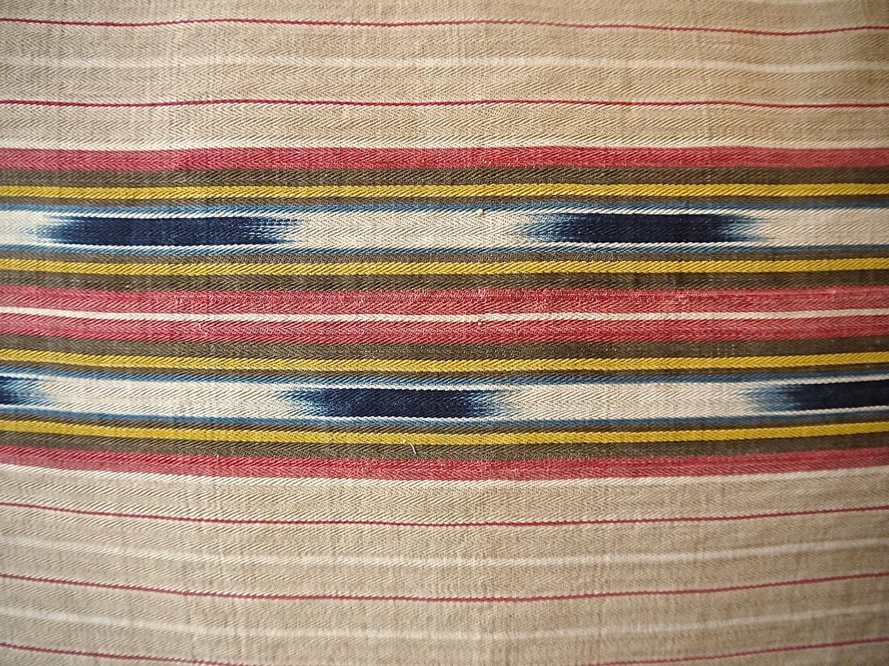French late 19th century unusual striped ticking linen cushion with an unusual indigo ikat detail in the stripe. Stripes of lightly faded beige, red and yellow with indigo ikat floating in between. With natural indigo dyed vintage French cotton