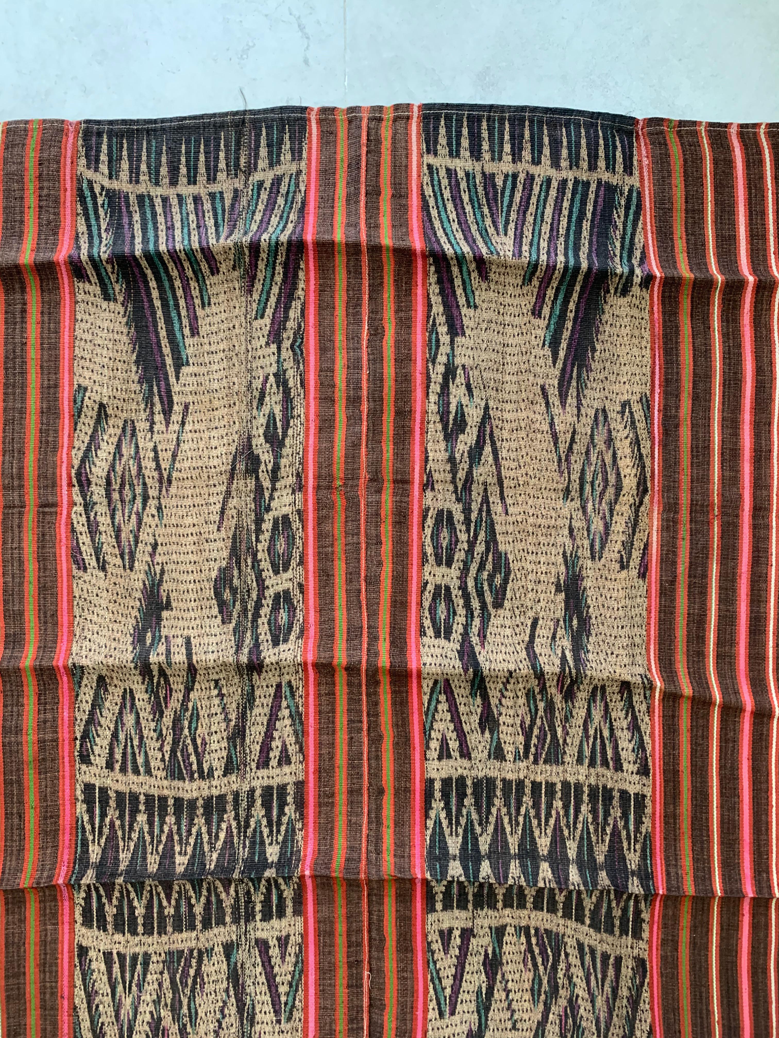 This Ikat textile originates from the Island of Kalimantan, Indonesia. It is hand-woven using naturally dyed yarns via a method passed on through generations amid the Dayak Tribes scattered throughout the island. It features a stunning orange, pink,